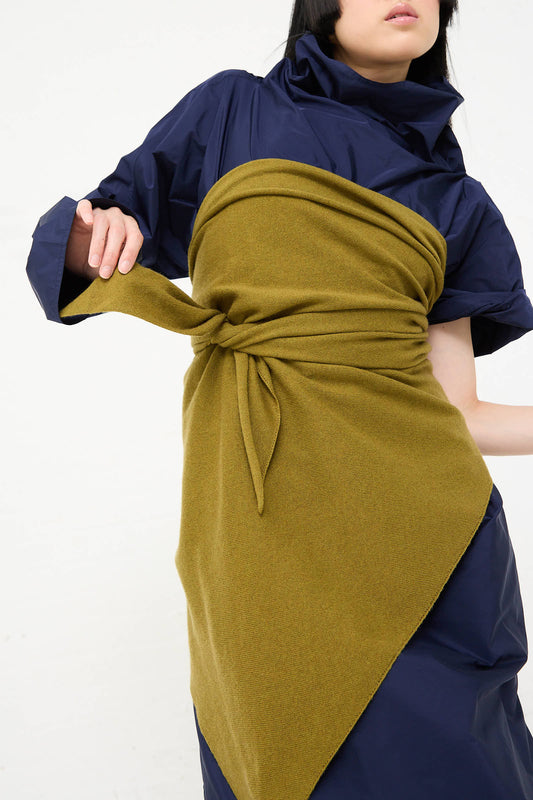 Person wearing a blue dress with the Sofie D'Hoore Wool Cashmere Astra Scarf in Olive wrapped around their torso, posing against a plain background.