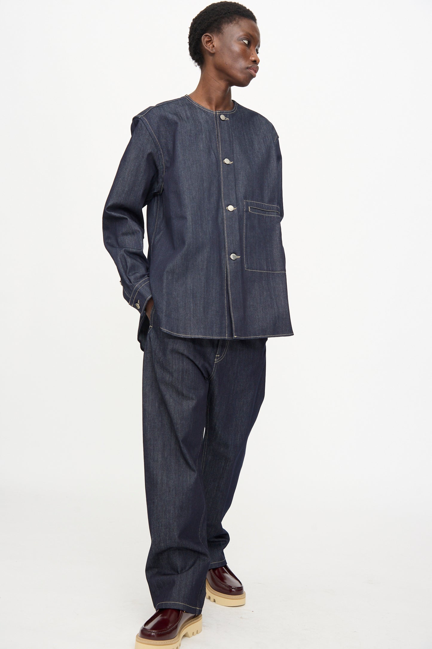 A person wearing the Sofie D'Hoore Barna Shirt in Midnight styled with matching wide-leg jeans and brown platform shoes stands against a plain white background.
