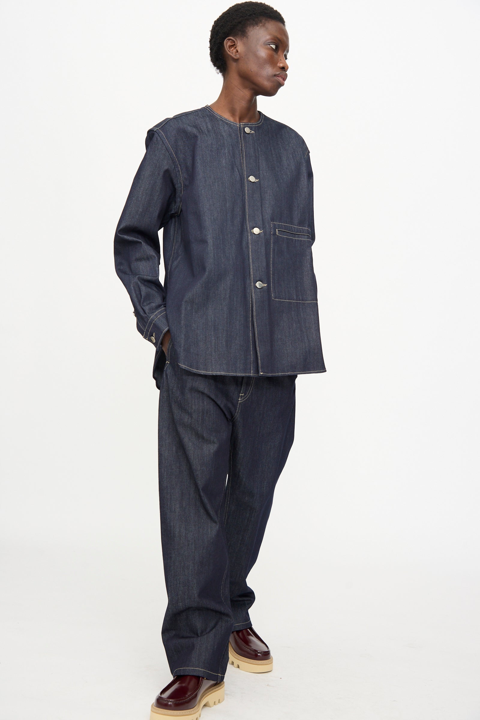 A person wearing the Sofie D'Hoore Barna Shirt in Midnight styled with matching wide-leg jeans and brown platform shoes stands against a plain white background.