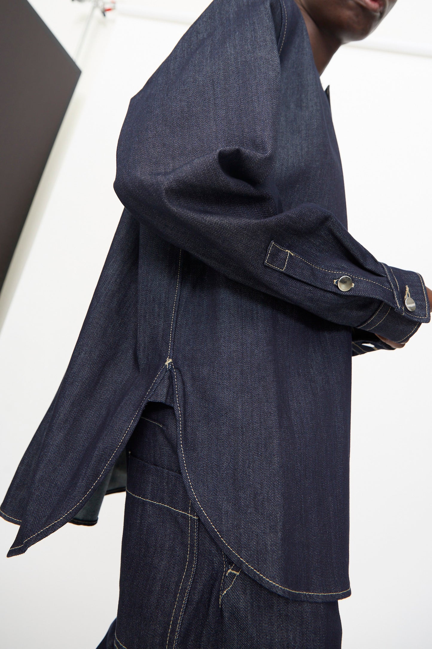 A person wears the Barna Shirt in Midnight by Sofie D'Hoore, featuring visible white stitching, side slits, and a relaxed fit for a stylish look.