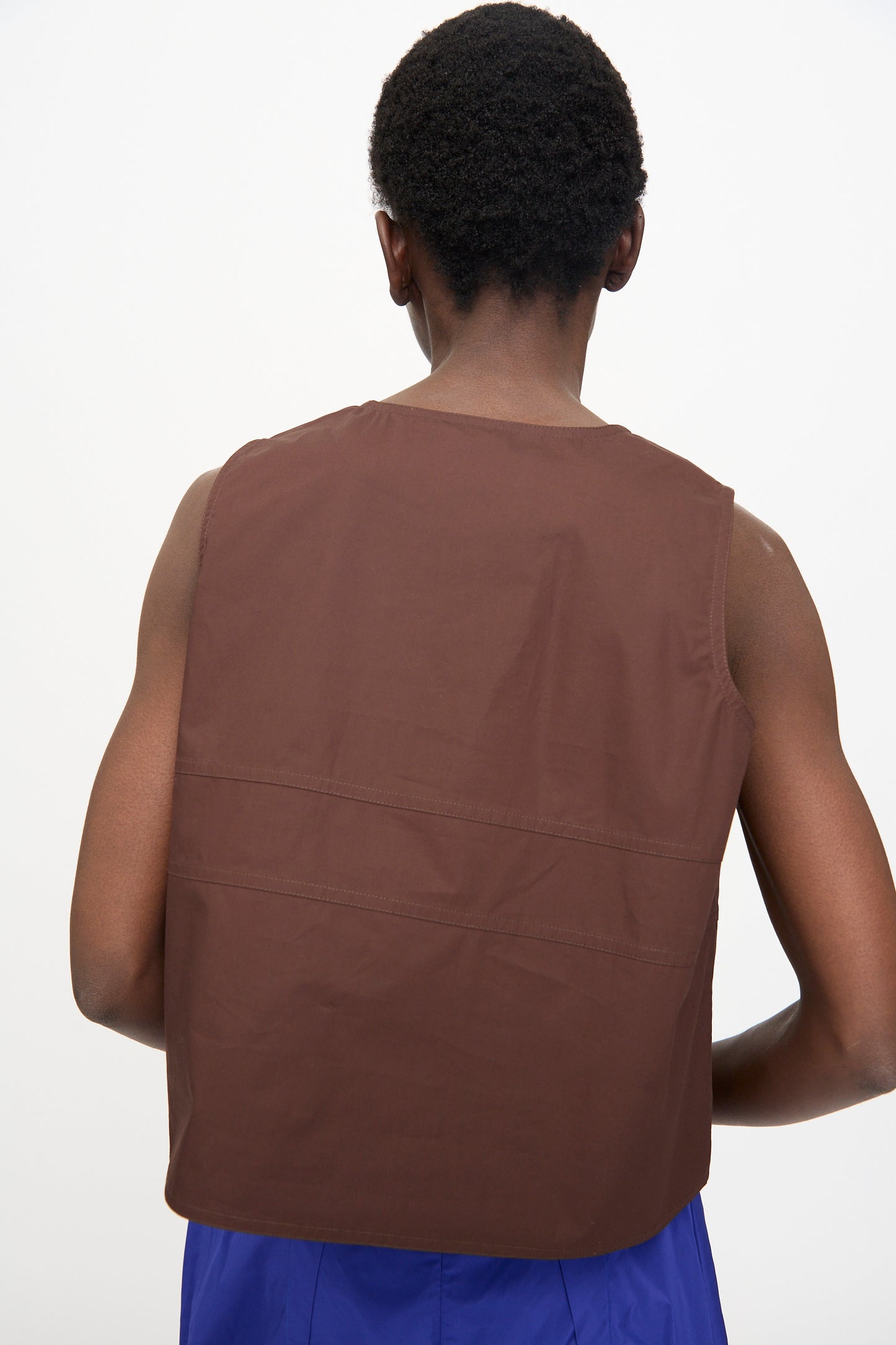 A person with short hair is shown from behind, wearing the Sofie D'Hoore Brambel Tank Shirt in Cacao and blue pants against a plain white background.