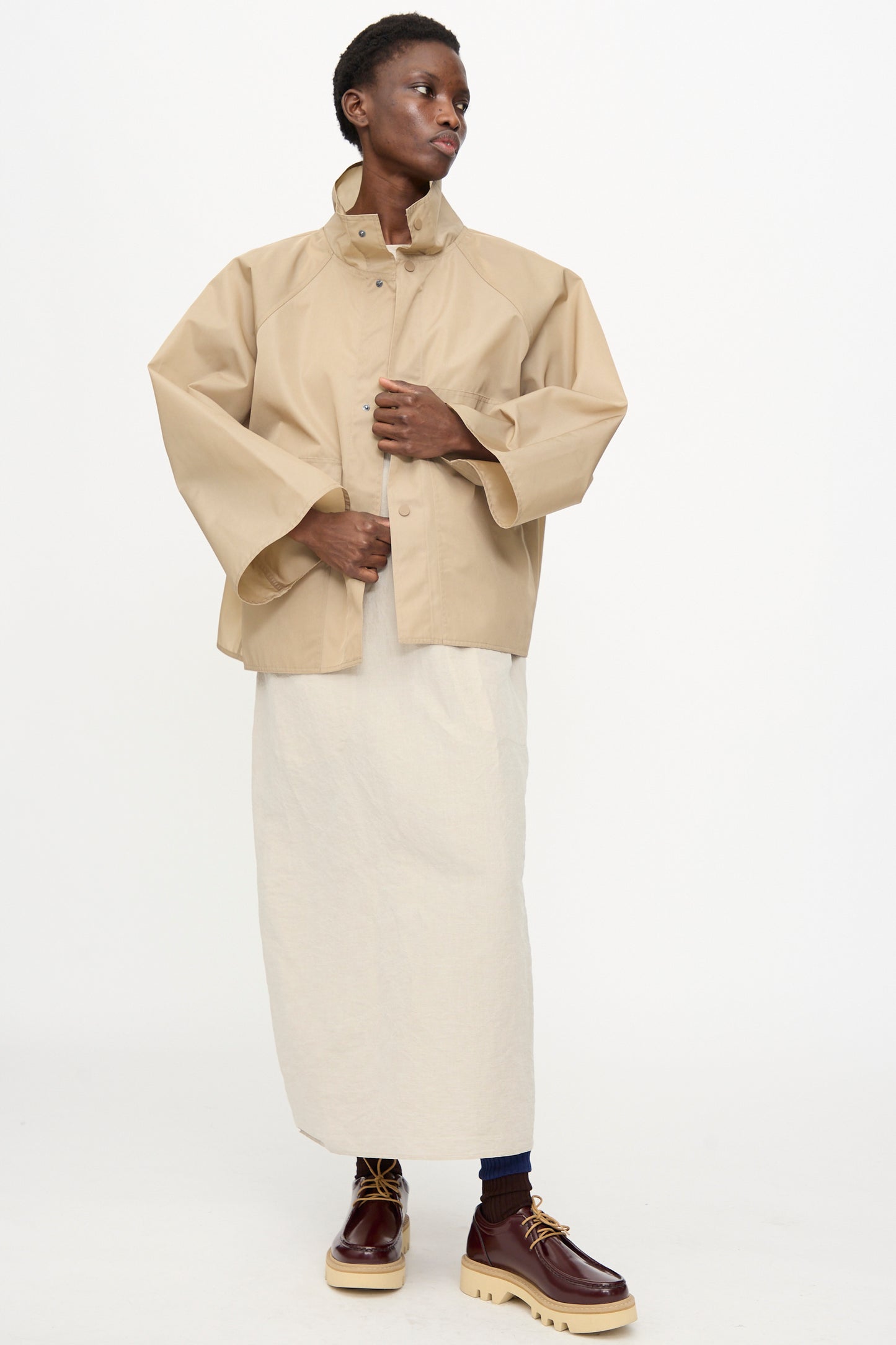 A person wears the Sofie D'Hoore Ceil Jacket in Moonstone, paired with a long off-white skirt and brown platform shoes, standing against a plain white background.