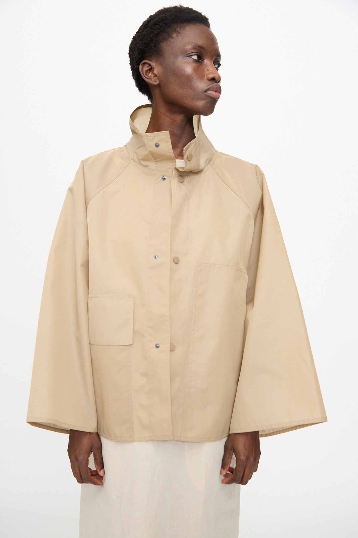 Model wearing the Sofie D'Hoore Ceil Jacket in Moonstone—an oversized beige taffeta canvas jacket with wide sleeves, high collar, and snap buttons—posed against a plain white background.