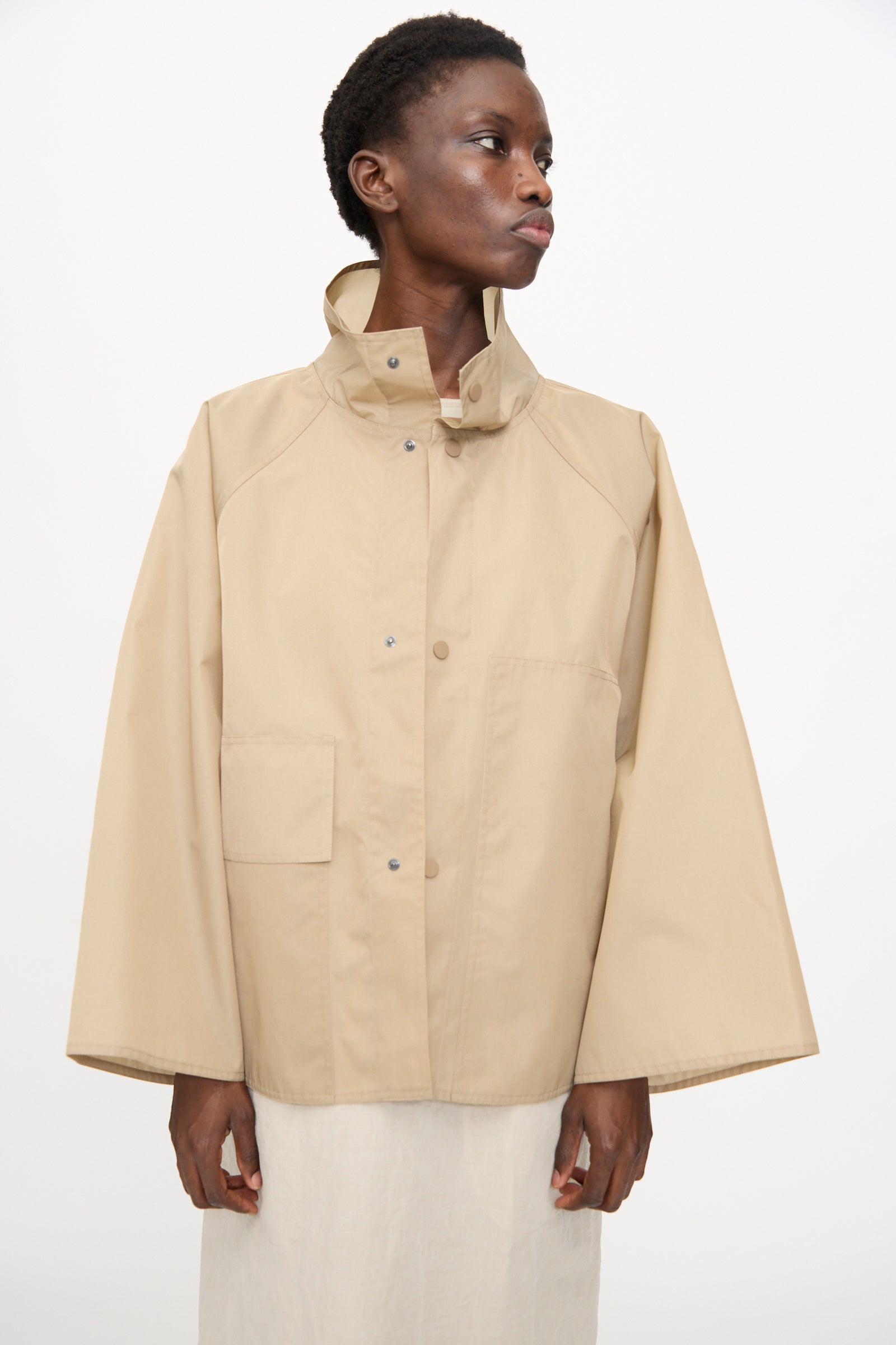 Model wearing the Sofie D'Hoore Ceil Jacket in Moonstone—an oversized beige taffeta canvas jacket with wide sleeves, high collar, and snap buttons—posed against a plain white background.