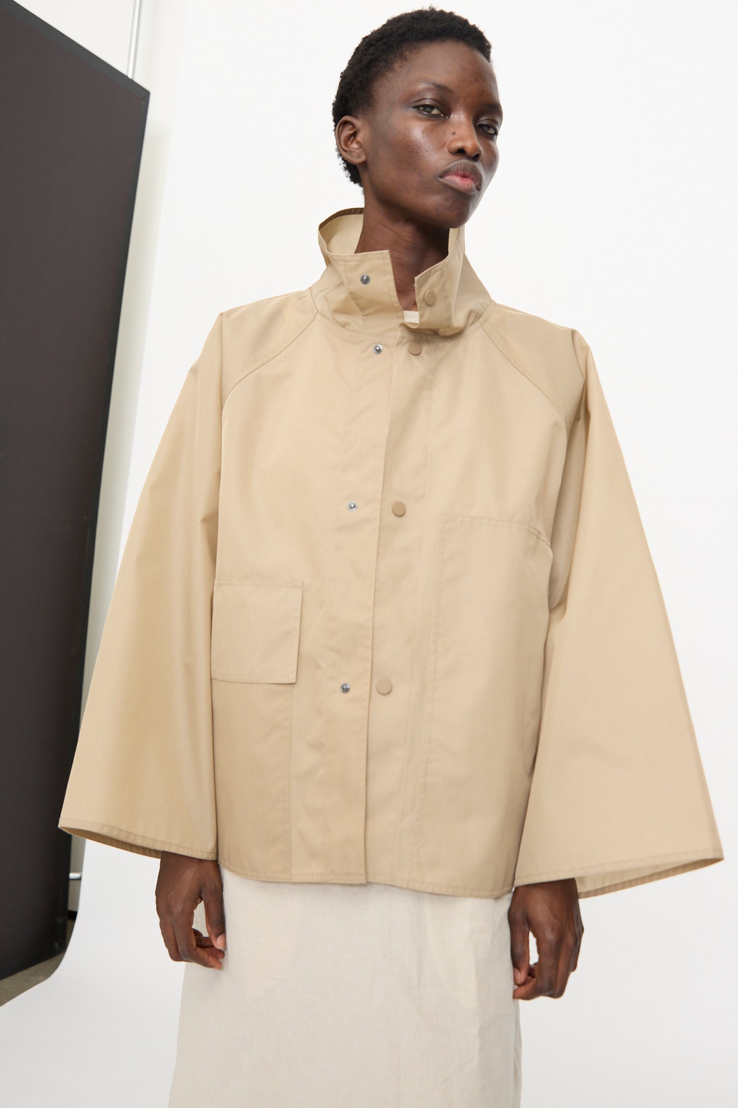 Person wearing the Sofie D'Hoore Ceil Jacket in Moonstone, a beige, water-repellent oversized jacket with wide sleeves and a large collar, standing against a plain background.