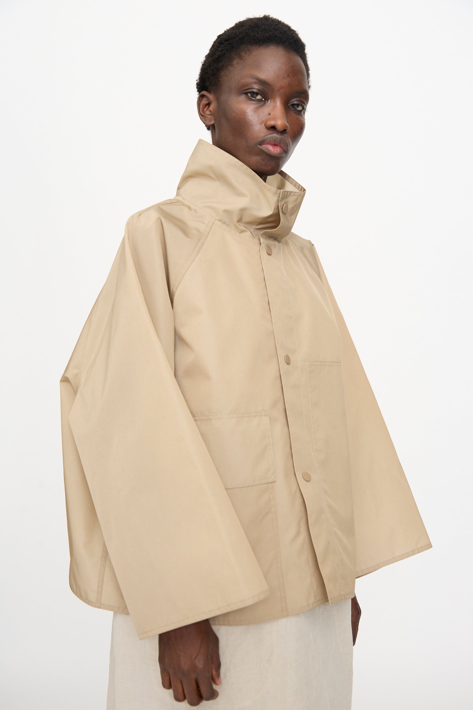 A person wearing the Sofie D'Hoore Ceil Jacket in Moonstone, an oversized light beige taffeta canvas jacket with wide sleeves and a high collar, over a light-colored outfit, standing against a plain white background.