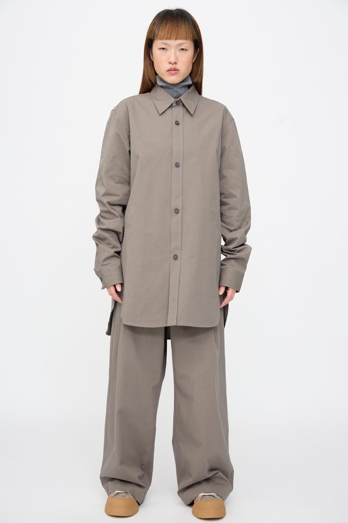 A person wearing a Brushed Cotton Voile Breg Shirt in Turtle over a grey turtleneck and matching wide-leg trousers, with chunky tan shoes.