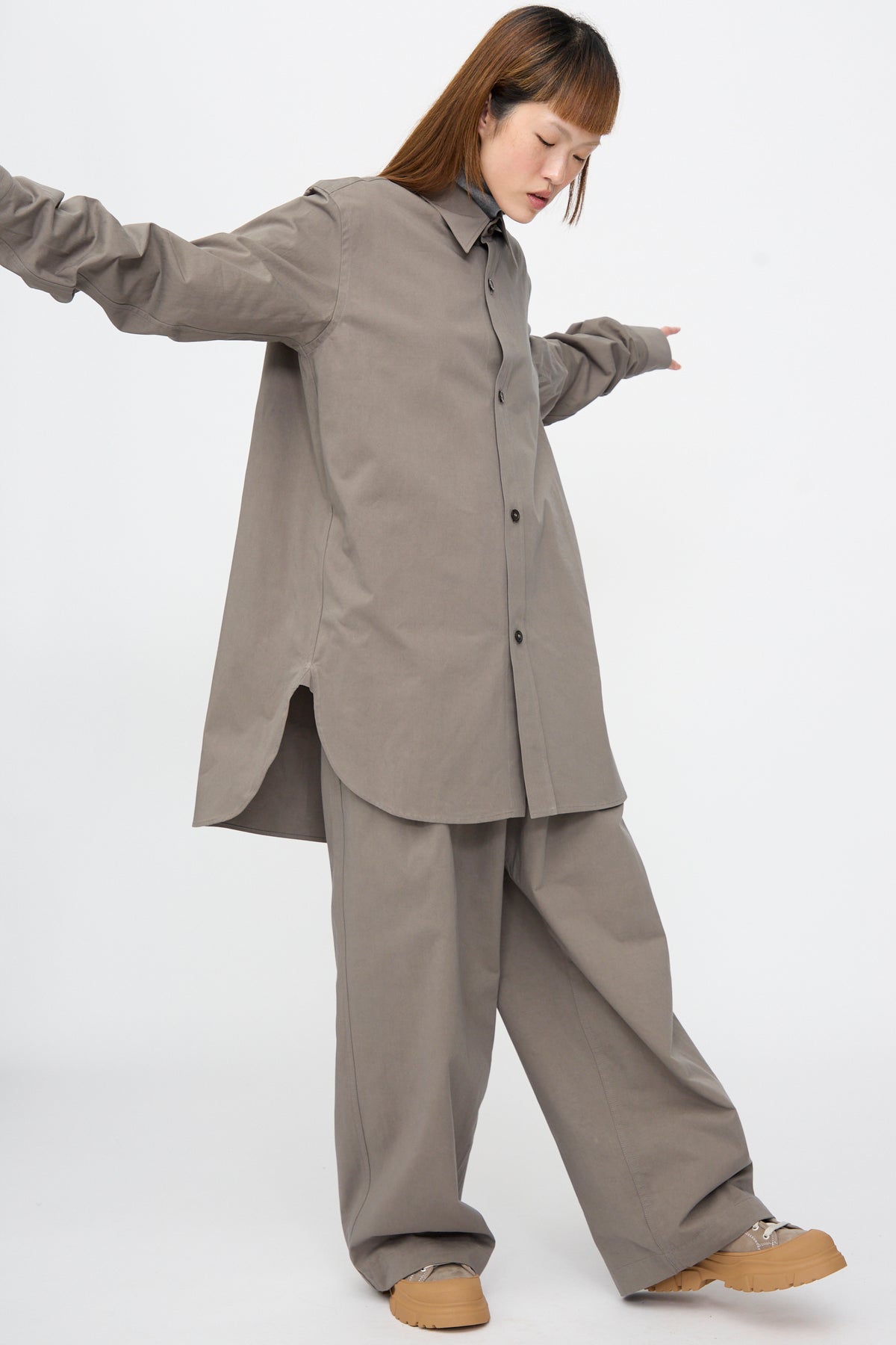 A person wearing a Brushed Cotton Voile Breg Shirt in Turtle and matching wide-leg trousers in grey, paired with beige sneakers.