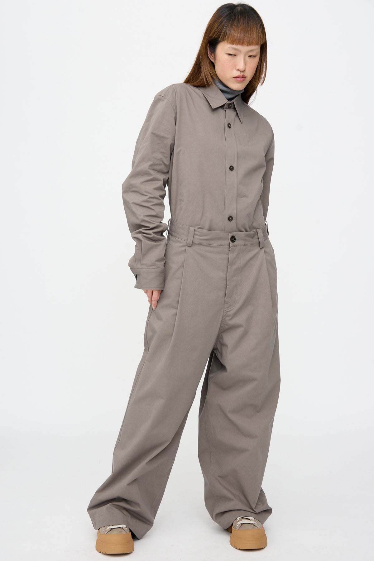 A person wearing a button-up shirt tucked into matching Compact Winter Cotton Pasadena Pant in Turtle, styled with a gray turtleneck and chunky tan sneakers.