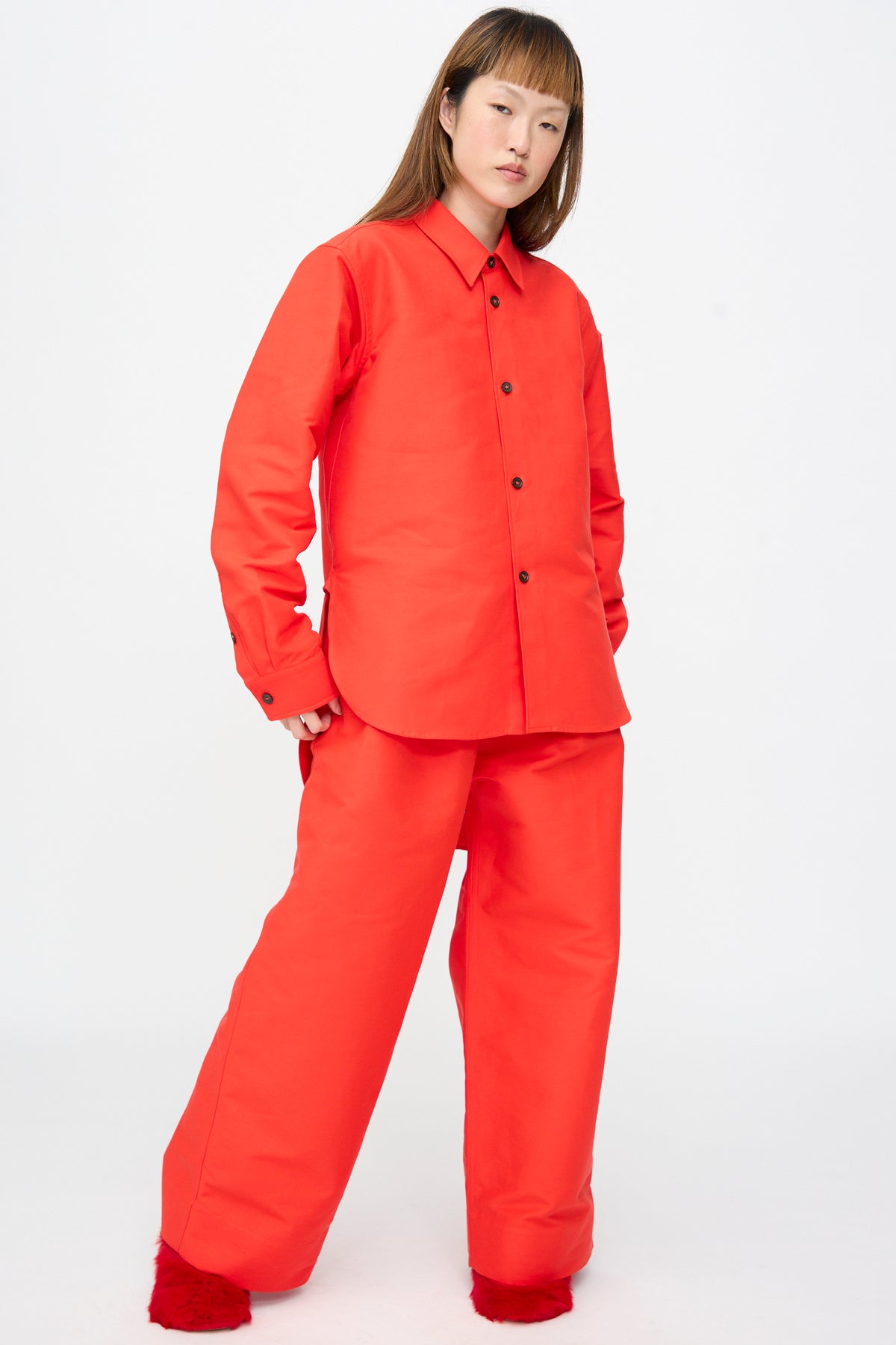 A person wearing an oversized bright red Cotton Duchesse Brant Shirt in Fire and matching wide-leg trousers.