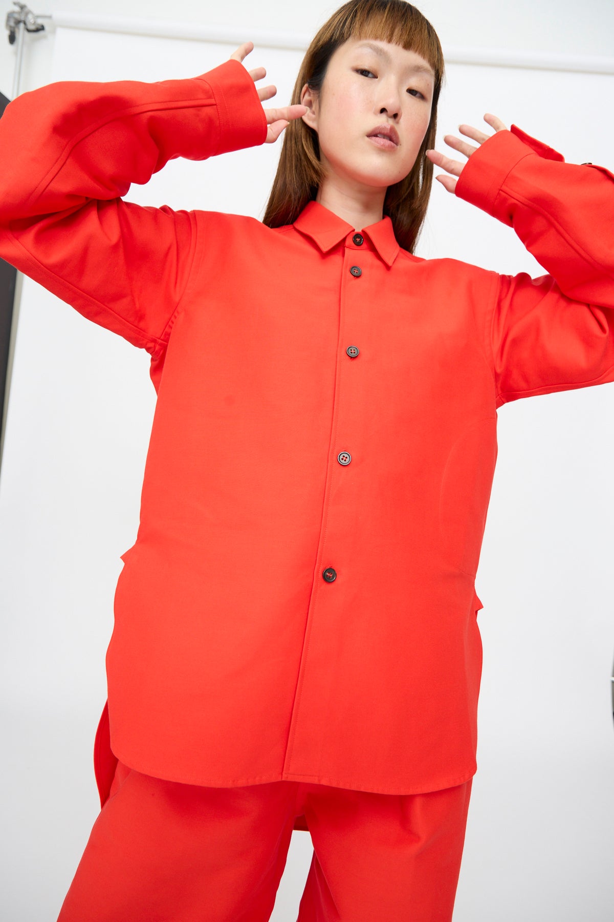 A model wearing a Sofie D’Hoore Cotton Duchesse Brant Shirt in Fire, an oversized, bright red long-sleeved button-down with a hi-low hem.