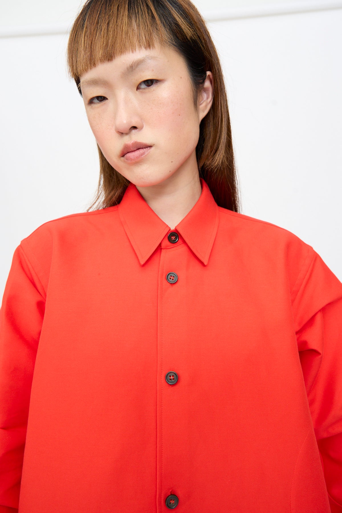 A person wearing an oversized bright red Cotton Duchesse Brant Shirt in Fire with long sleeves, dark buttons, and a hi-low hem.