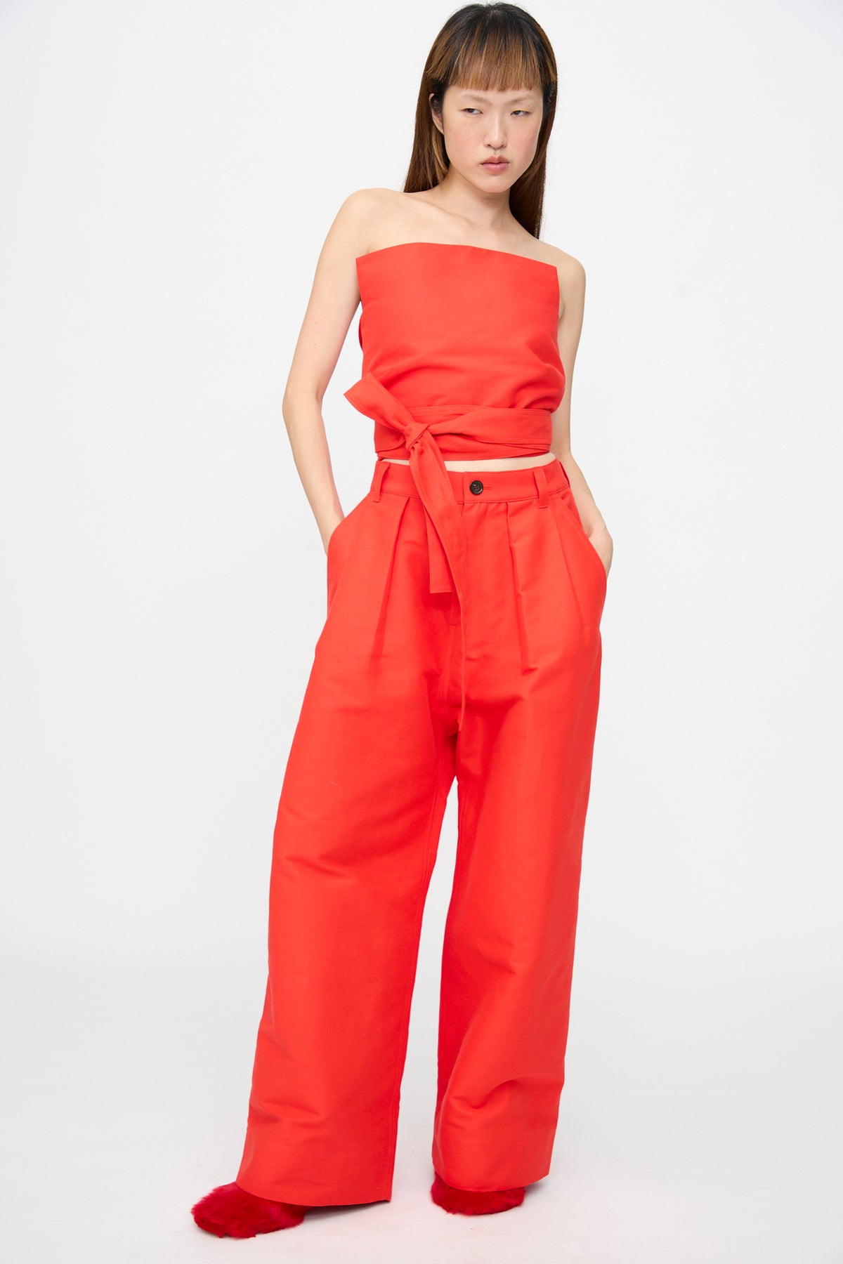 A person wearing a bright red Cotton Duchesse Brel Shirt in Fire cropped tube top and matching high-waisted wide-leg trousers.