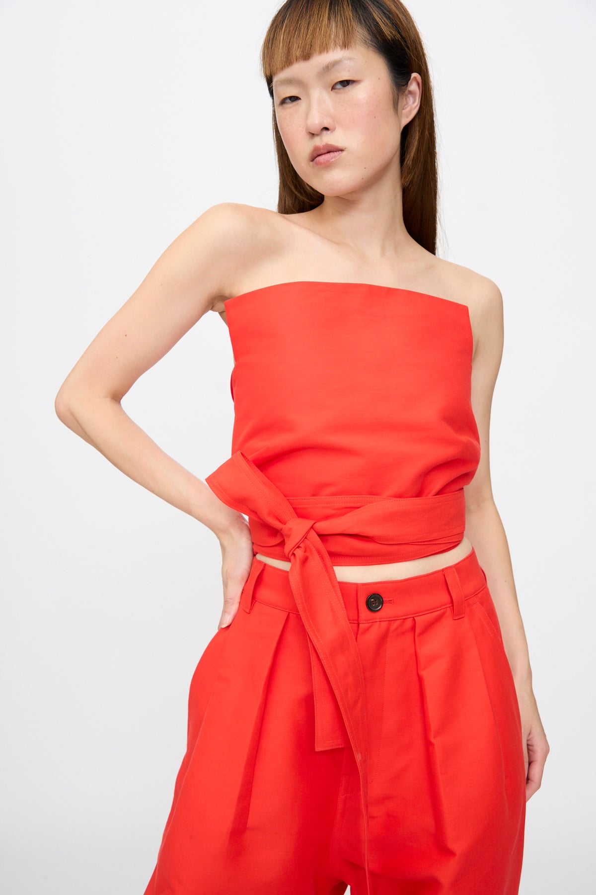 Model wearing a bright red Cotton Duchesse Brel Shirt in Fire cropped tube top with a wrap-around tie waist and matching trousers.