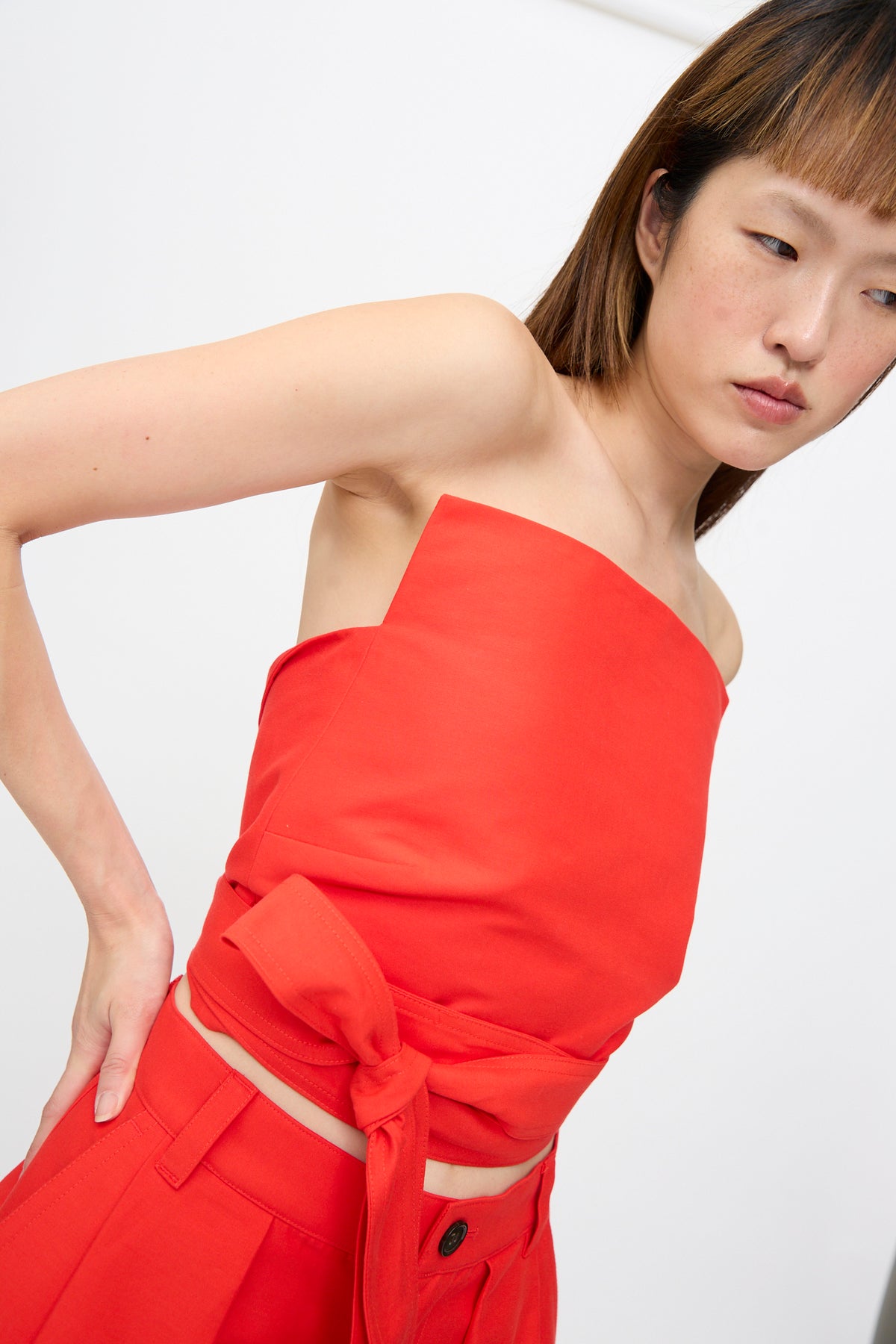 A woman wears a bright red Cotton Duchesse Brel Shirt in Fire cropped tube top with a wrap-around tie waist and matching red trousers.