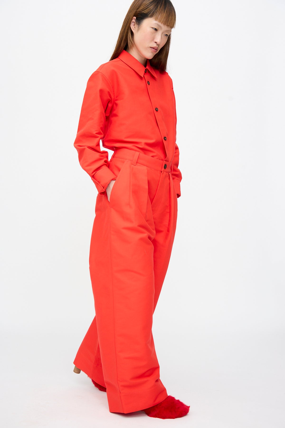 A person wearing a bright red, oversized button-down shirt tucked into matching Cotton Duchesse Piaf Pant in Fire wide-leg trousers by Sofie D’Hoore.