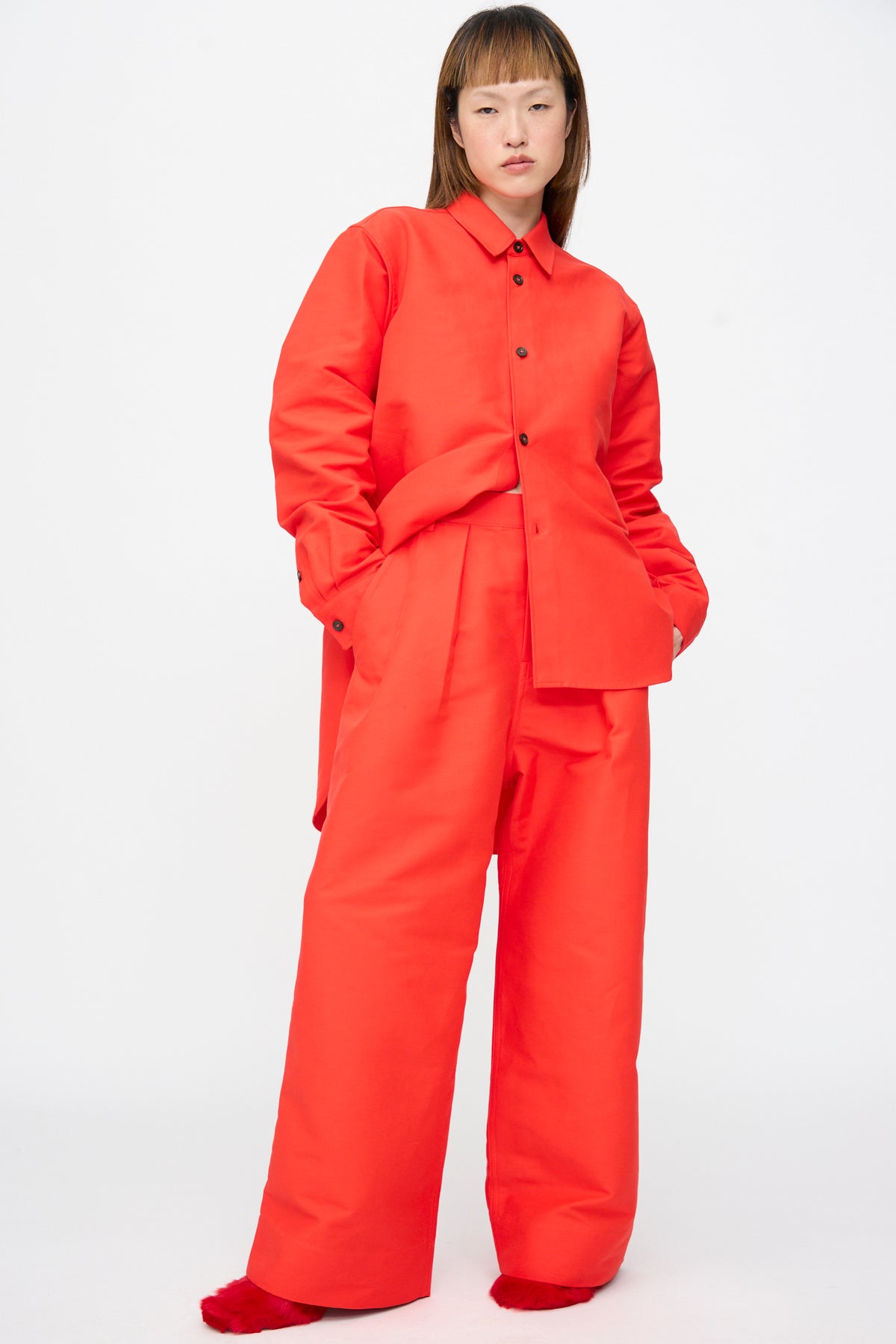 A person wearing an oversized bright red button-down shirt and matching Sofie D’Hoore Cotton Duchesse Piaf Pant in Fire featuring wide-leg trousers with front pleats.