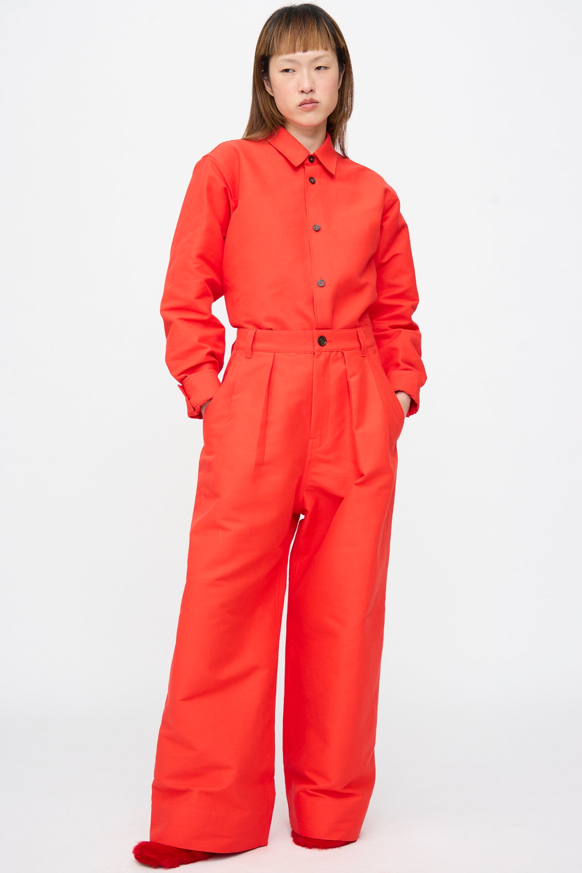A person wearing a bright red long-sleeved button-down shirt and matching Sofie D’Hoore Cotton Duchesse Piaf Pant in Fire, styled as high-waisted, oversized wide-leg trousers with front pleats.