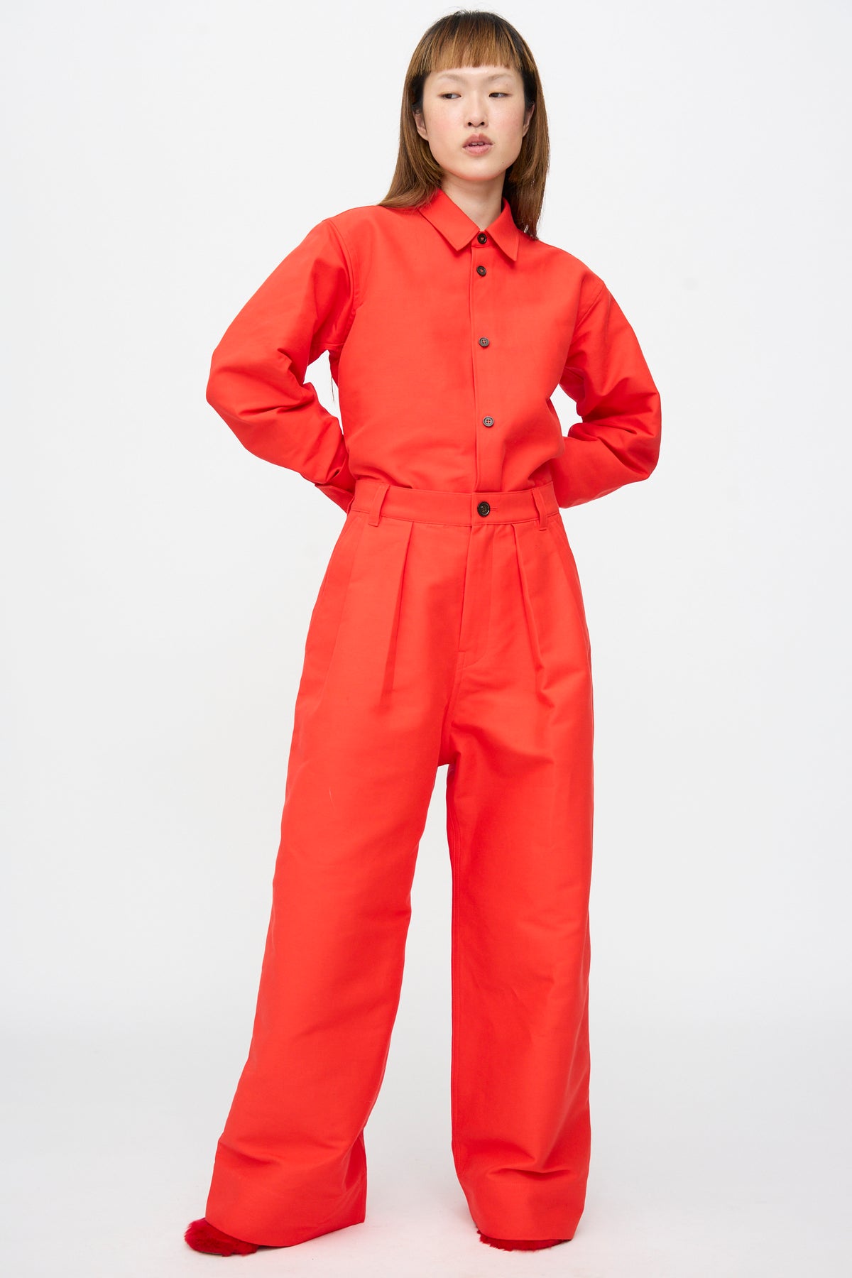 A person wearing a bright red long-sleeve button-up shirt tucked into matching Sofie D’Hoore Cotton Duchesse Piaf Pant in Fire high-waisted wide-leg trousers.