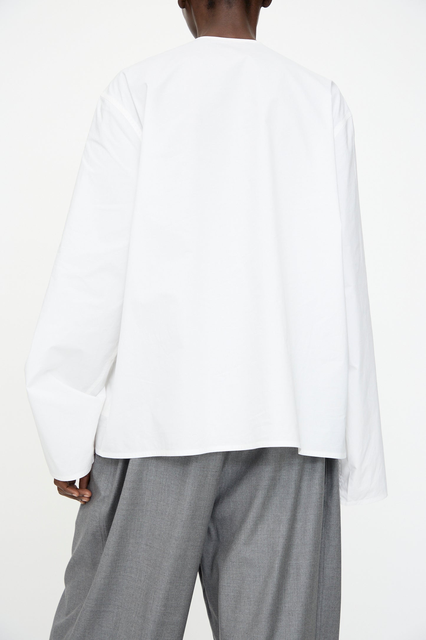 A person is shown from the back, wearing the Sofie D'Hoore Cotton Poplin Balthus Shirt in white with gray wide-leg pants against a plain white background.