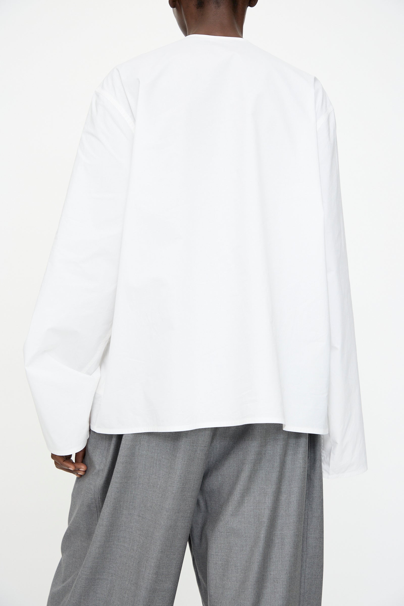 A person is shown from the back, wearing the Sofie D'Hoore Cotton Poplin Balthus Shirt in white with gray wide-leg pants against a plain white background.
