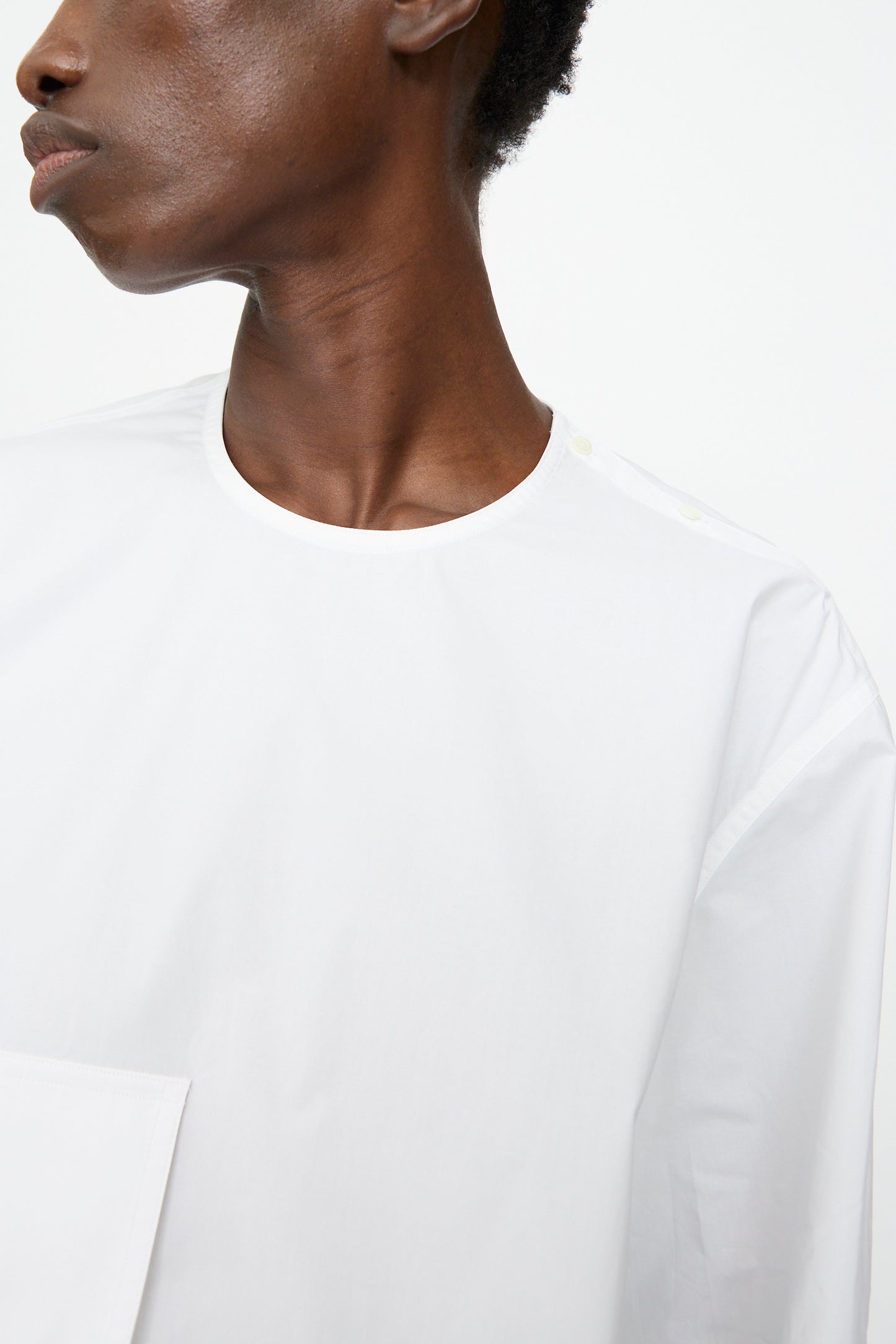 A person wears the Sofie D'Hoore Cotton Poplin Balthus Shirt in White, featuring an oversized fit and round neckline, shown from the shoulders up against a white background.