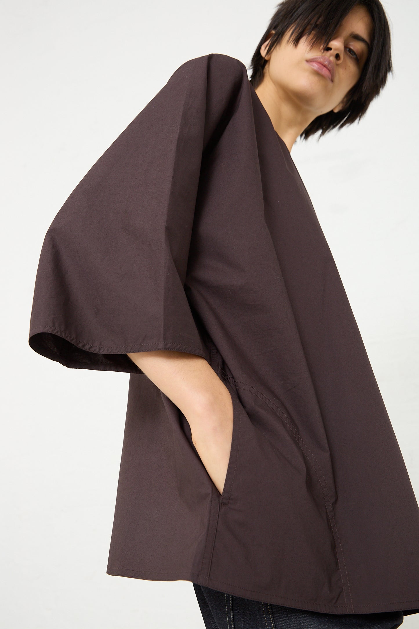 The model is wearing a brown-colored Cotton Poplin Bendol Top by Sofie D'Hoore, with side seam pockets, featuring an oversized fit. Side view.