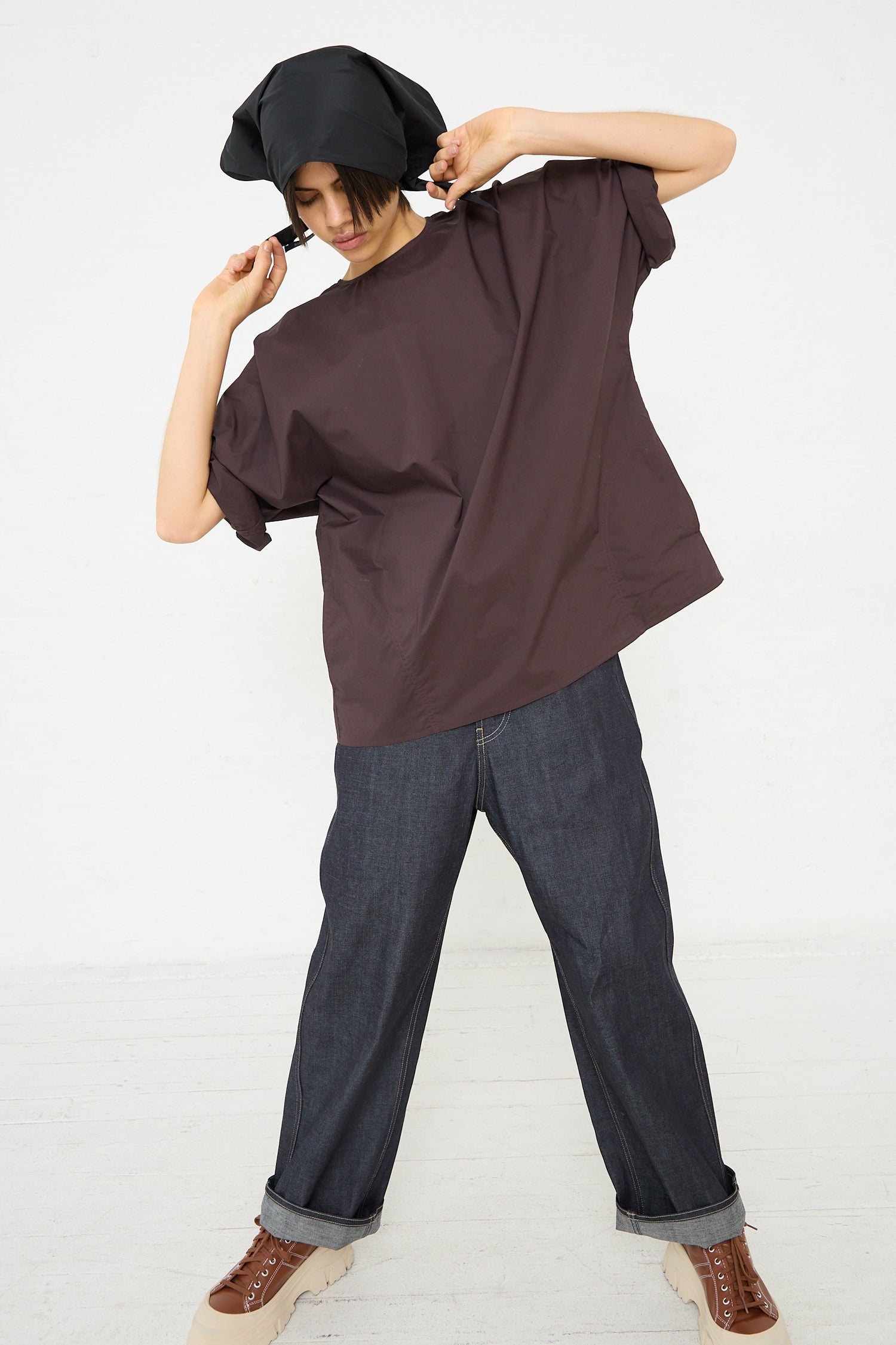 An oversized fit Cotton Poplin Bendol Top with Scarf in Ebony by Sofie D'Hoore, with side seam pockets, worn by a woman and jeans. Full length and front view.