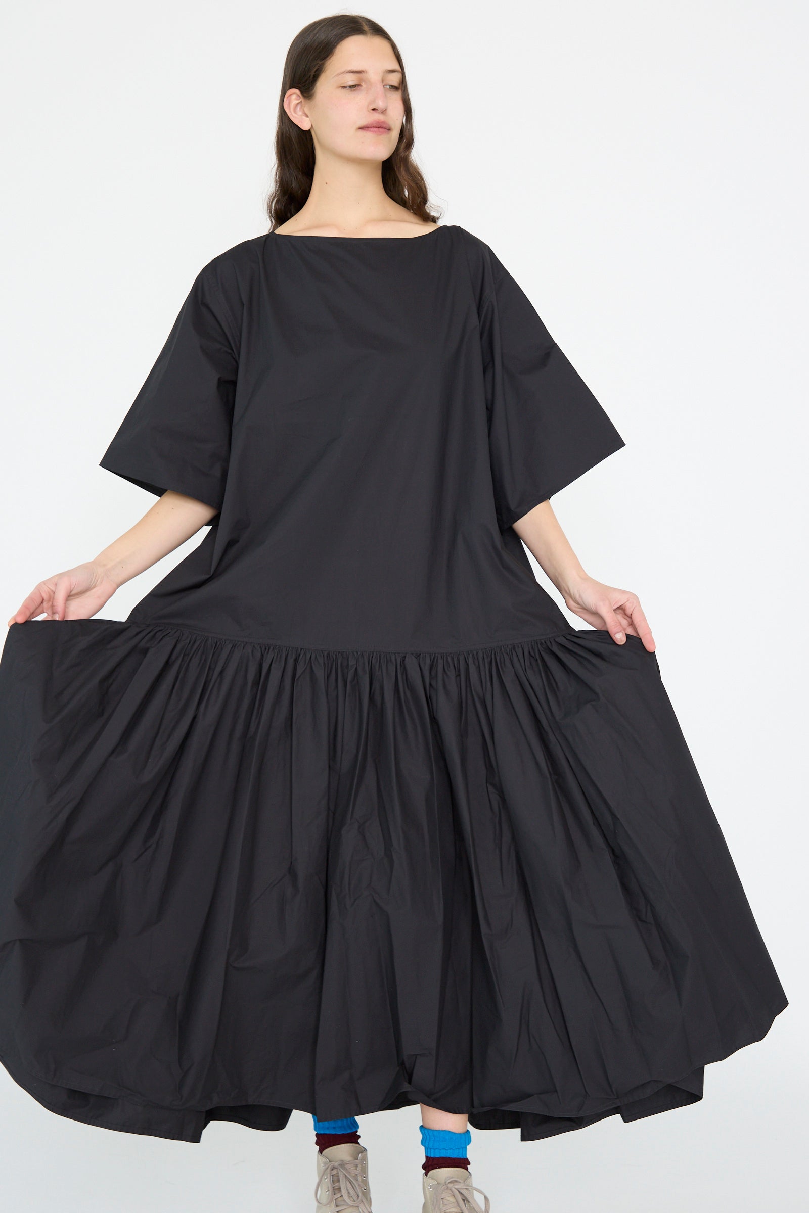 A person stands against a plain background in the Cotton Poplin Della Dress by Sofie D'Hoore, showcasing its oversized design with wide sleeves and a voluminous skirt in black.