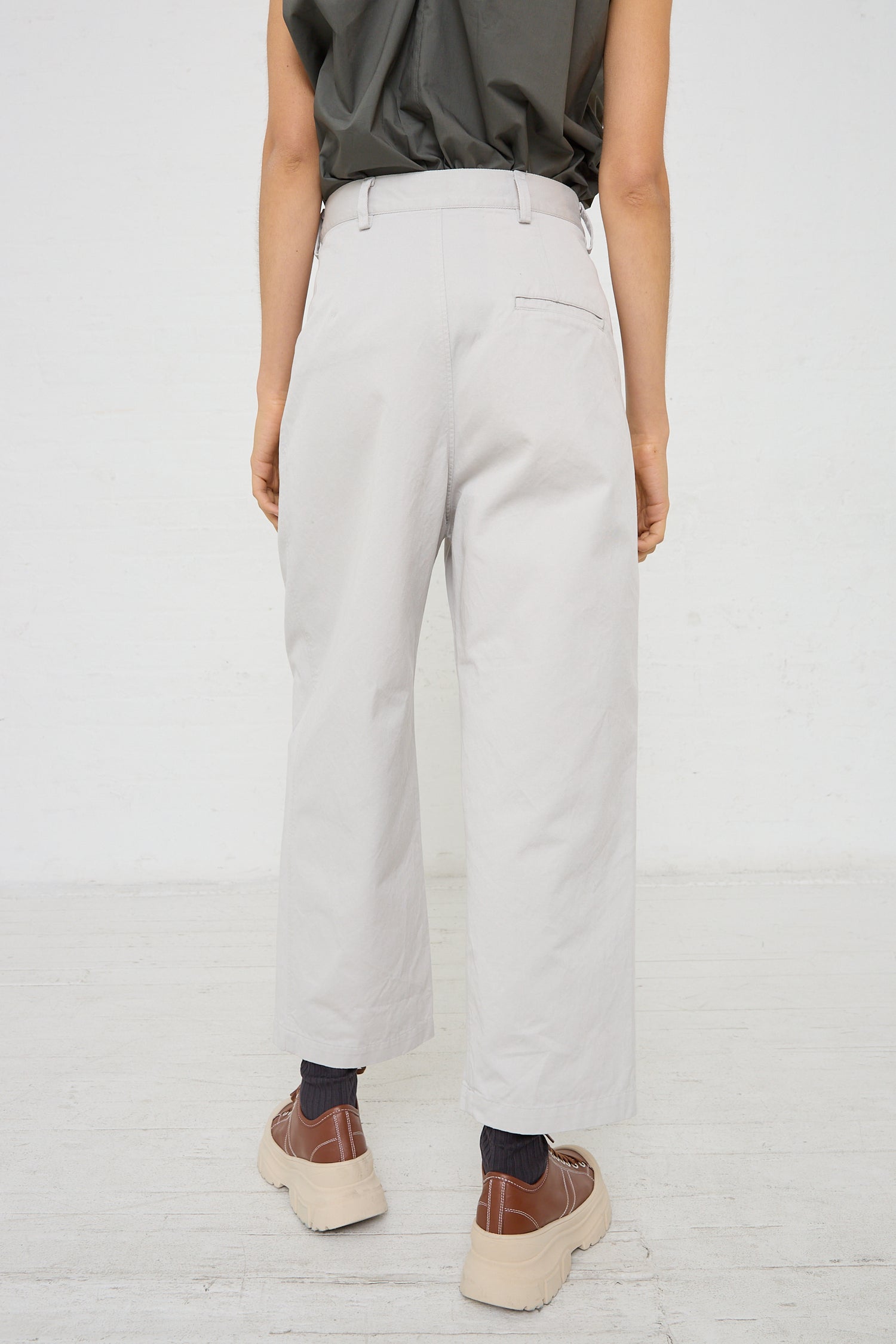 The back view of a woman wearing a low-rise, Sofie D'Hoore Cotton Twill Proof Pant in Mastic with pleat detail.