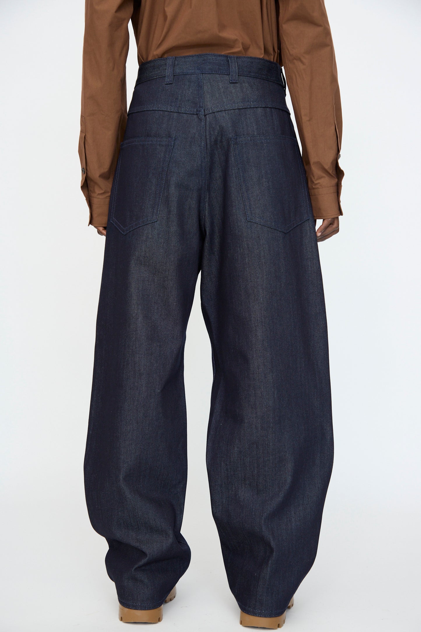 A person wearing the Sofie D'Hoore Denim Peggy Pant in Raw with a brown long-sleeve shirt, facing away from the camera against a plain background.