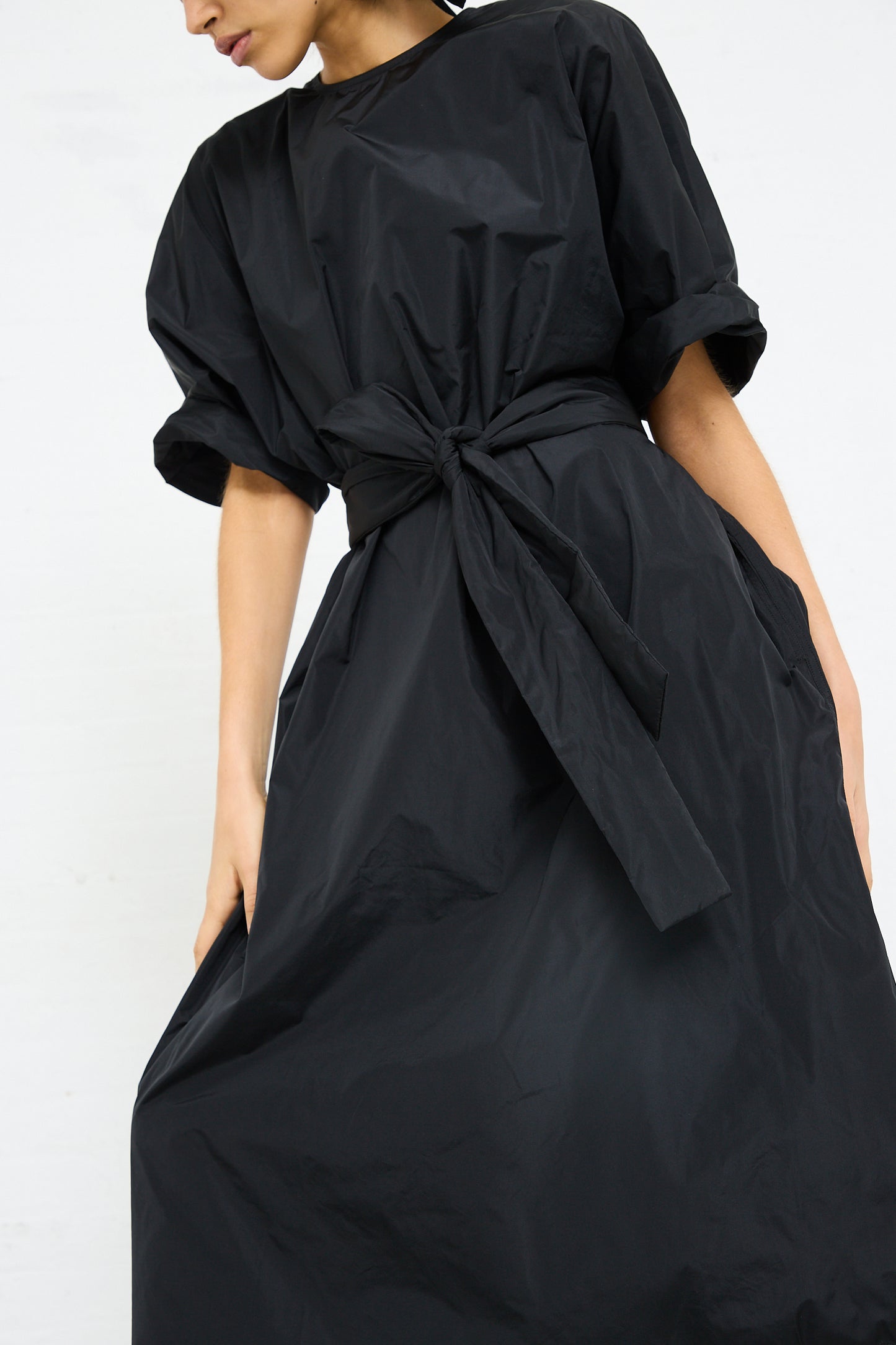 Woman in a Sofie D'Hoore Duke Dress with Lace Hem in Black with a tied waist detail.