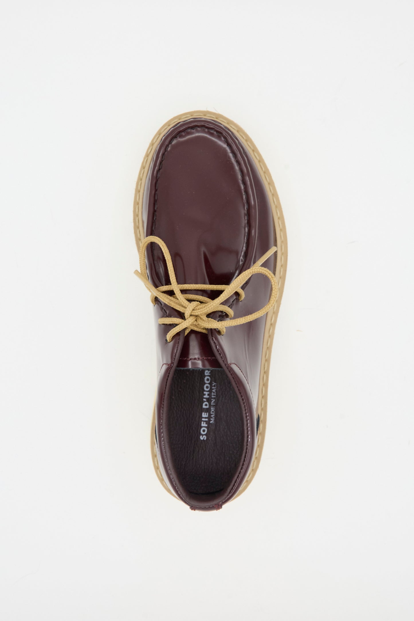 The Falcone Wallabee Shoe in Mahogany by Sofie D'Hoore features rich maroon patent leather, tan laces, and a beige rubber sole, shown from above on a white background.