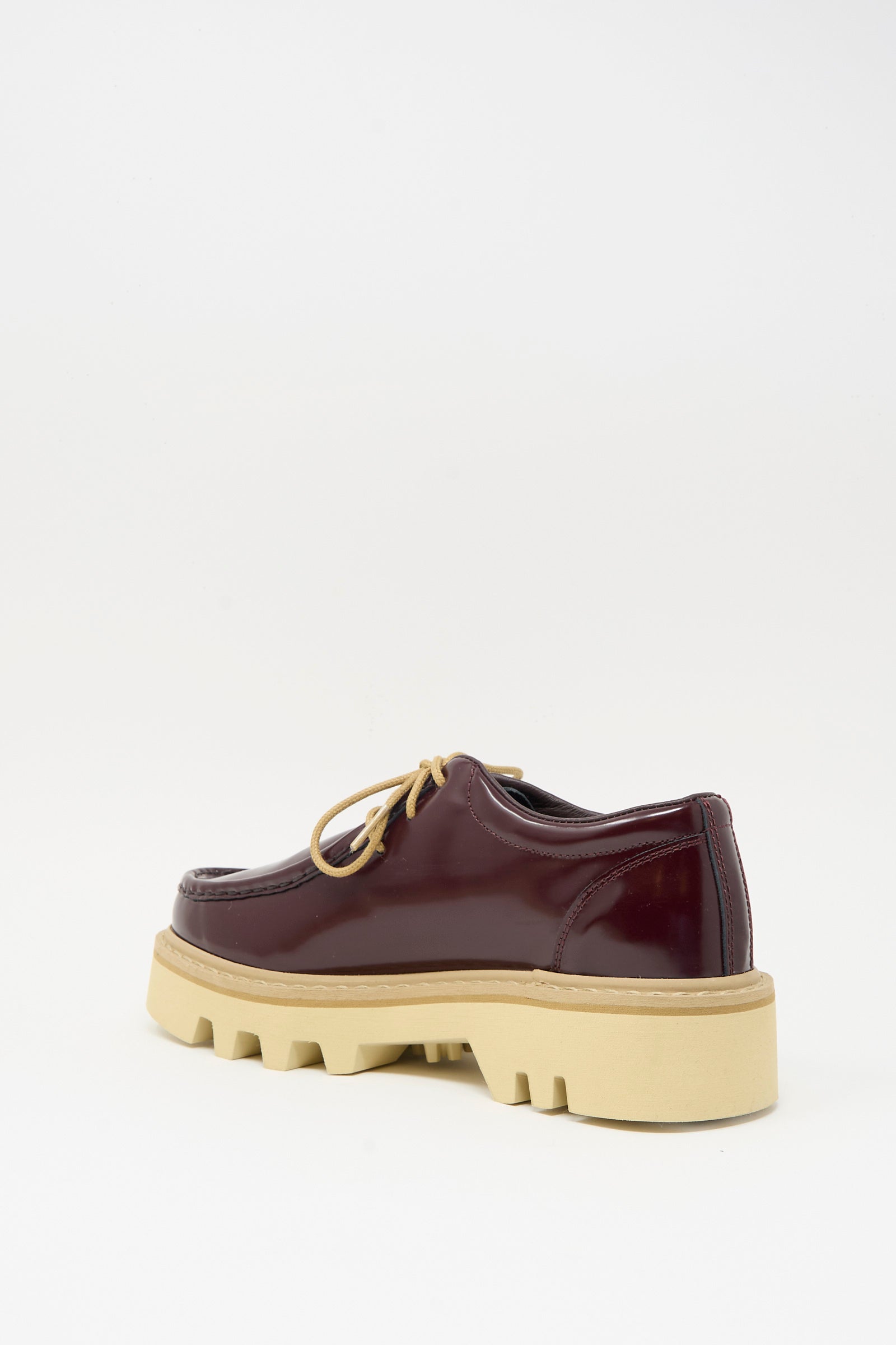 The Falcone Wallabee Shoe in Mahogany by Sofie D'Hoore features burgundy patent leather, lace-up design, and a thick beige rubber sole, shown from a rear angled view on a white background.