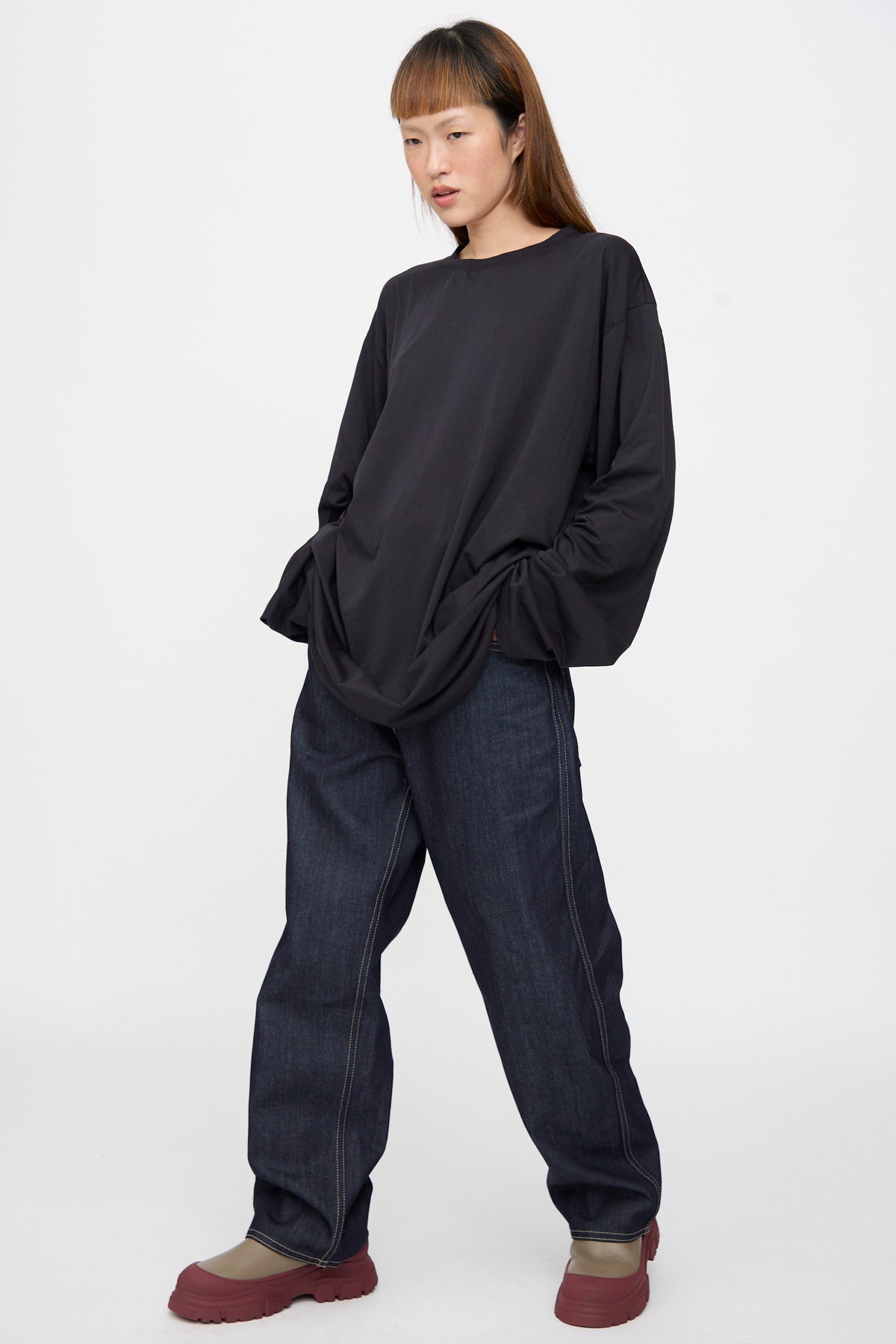 A person wears a Sofie D’Hoore Fine Cotton Jersey Toledo Tee in Cosmos, dark denim jeans with contrast stitching, and taupe shoes with thick soles.