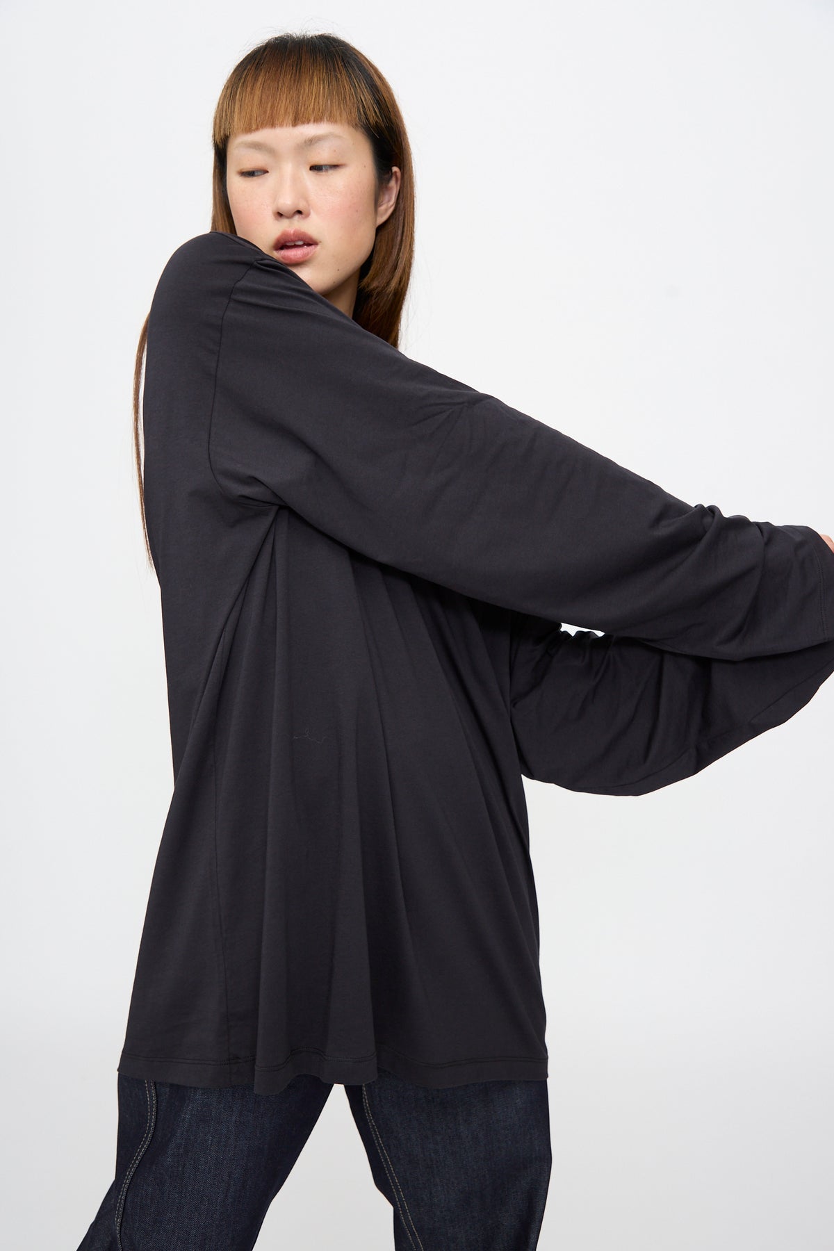 A person wearing a black Sofie D’Hoore Fine Cotton Jersey Toledo Tee in Cosmos with wide, flared sleeves and dark denim jeans.