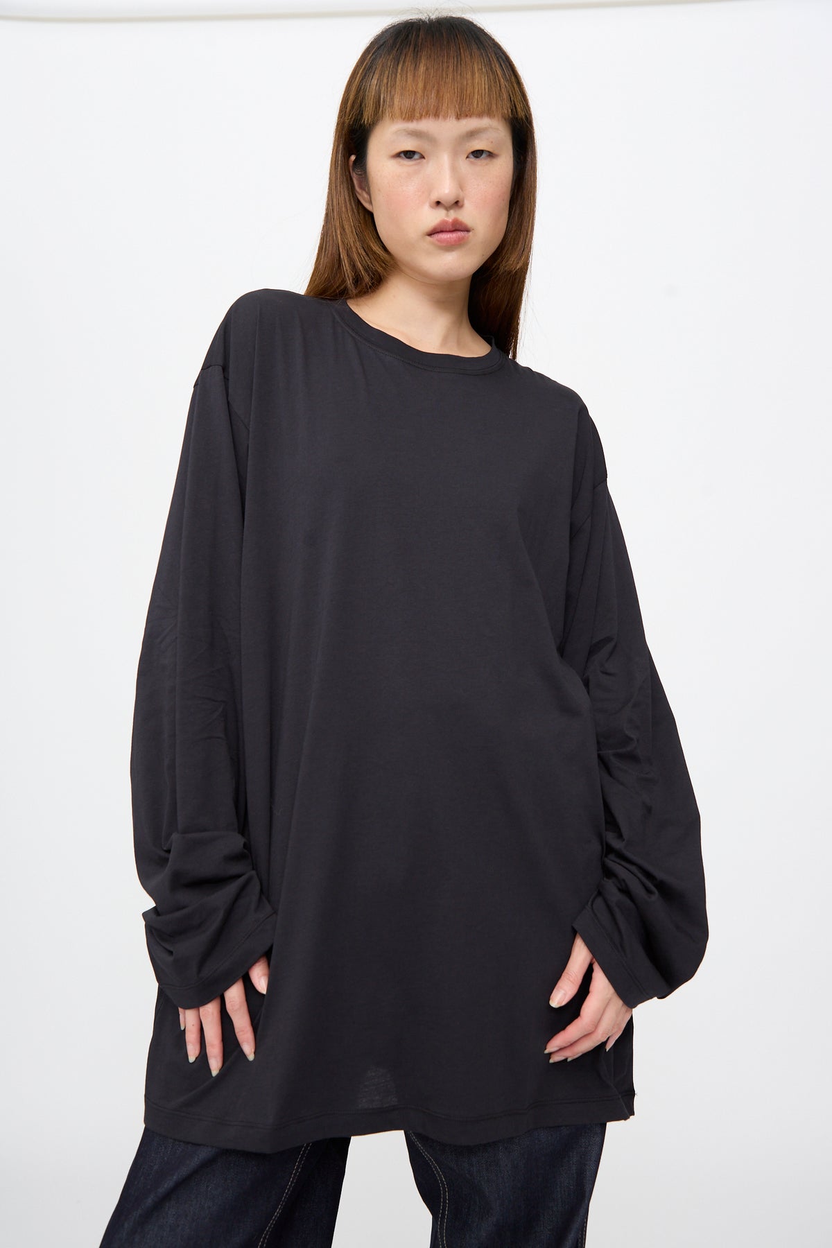A person wearing an oversized black Fine Cotton Jersey Toledo Tee in Cosmos with long sleeves.