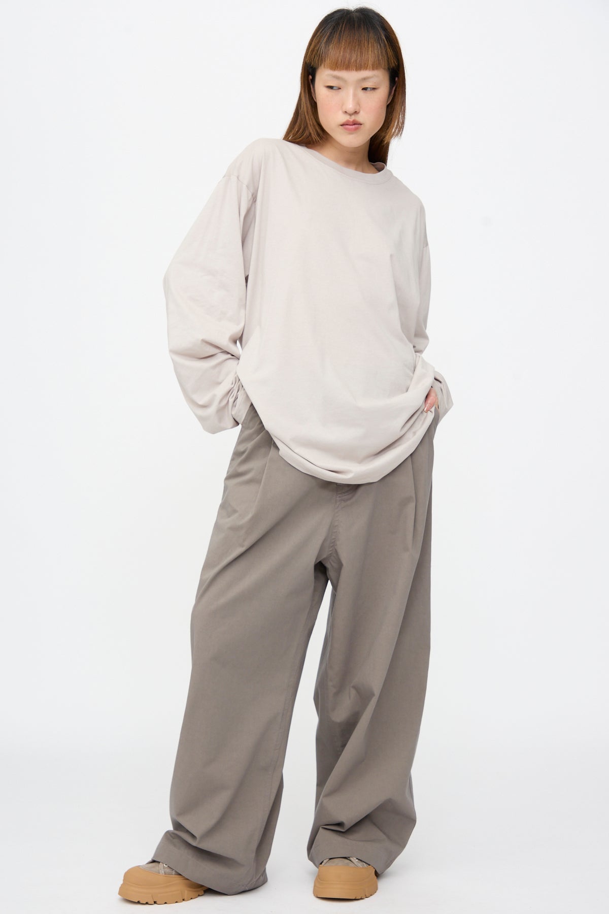 A person wearing an oversized light beige Fine Cotton Jersey Toledo Tee in Powder, wide-leg grey trousers, and tan platform sneakers.