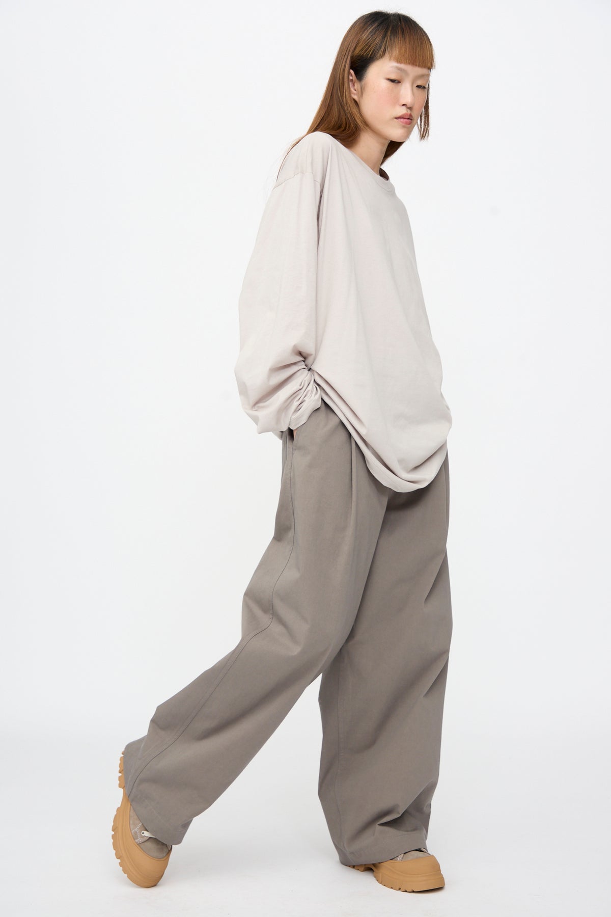 A person wearing a light beige Fine Cotton Jersey Toledo Tee in Powder, wide-leg taupe trousers, and beige sneakers with thick rubber soles.