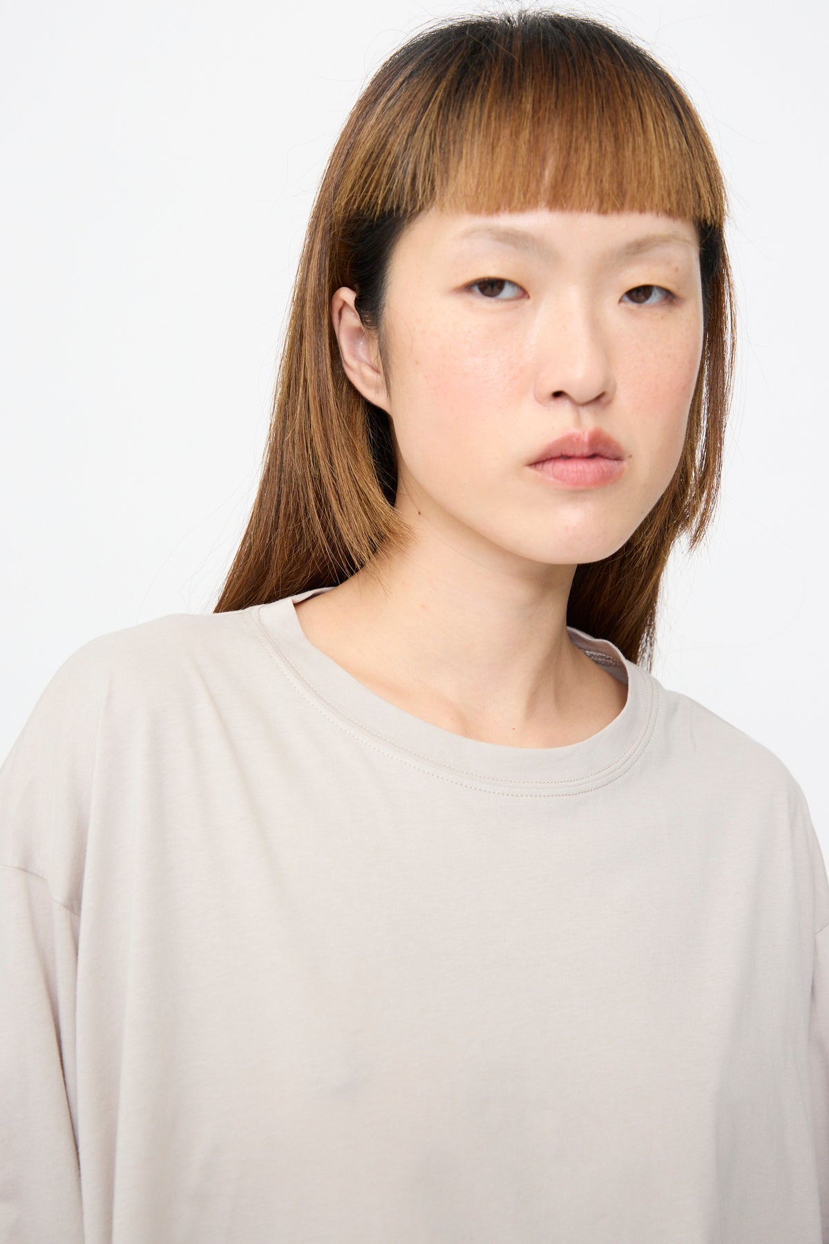 A person wearing a Sofie D’Hoore Fine Cotton Jersey Toledo Tee in Powder, an oversized, light beige cotton jersey crewneck t-shirt.