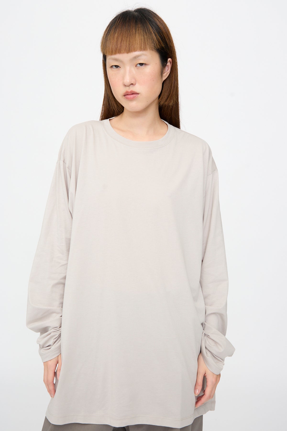 A person wearing a light gray, oversized Sofie D’Hoore Fine Cotton Jersey Toledo Tee in Powder, featuring a crew neckline and long sleeves.