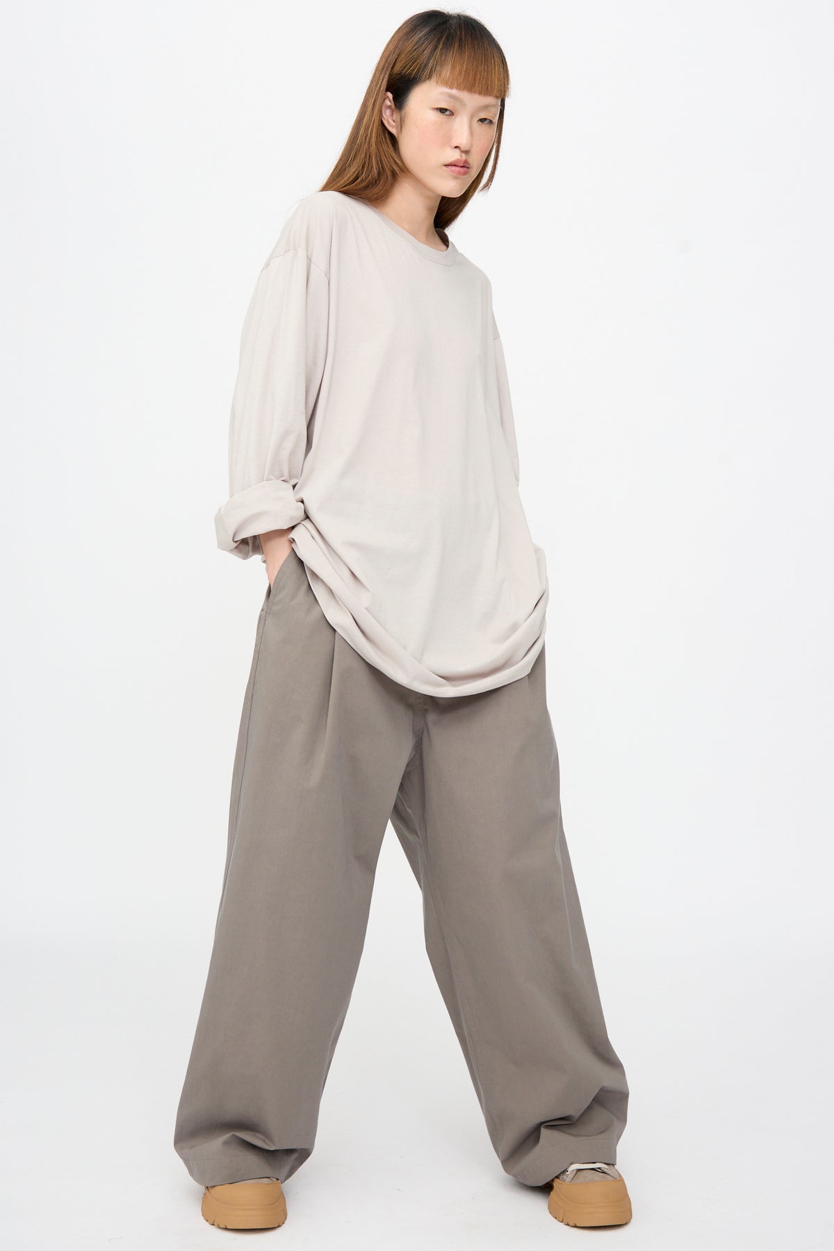 A person wearing a light beige Fine Cotton Jersey Toledo Tee in Powder and wide-leg grey trousers.