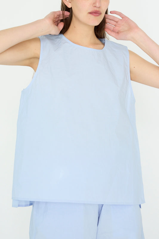 A person in a Glazed Cotton Brody Top in Sky by Sofie D'Hoore adjusts their hair against a white background. 