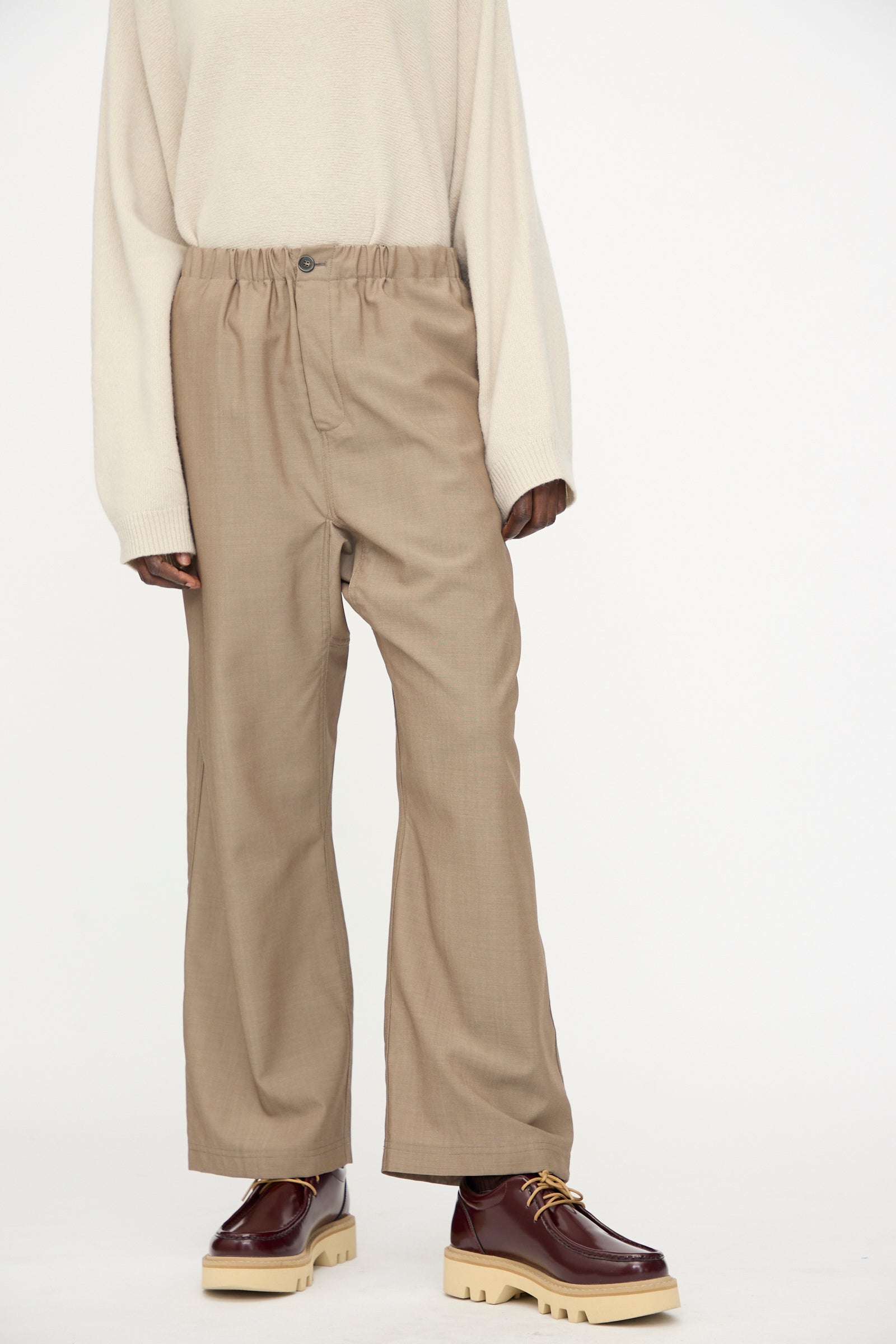 A person wears the Sofie D'Hoore Light Mohair Wool Pinot Pant in Quartz, a loose cream sweater, and chunky brown shoes with thick beige soles, standing against a plain white background.