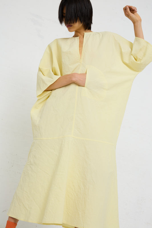 A person in a flowing yellow oversized Linen Cotton Delfi Dress in Pastis from Sofie D'Hoore posing with one arm raised.