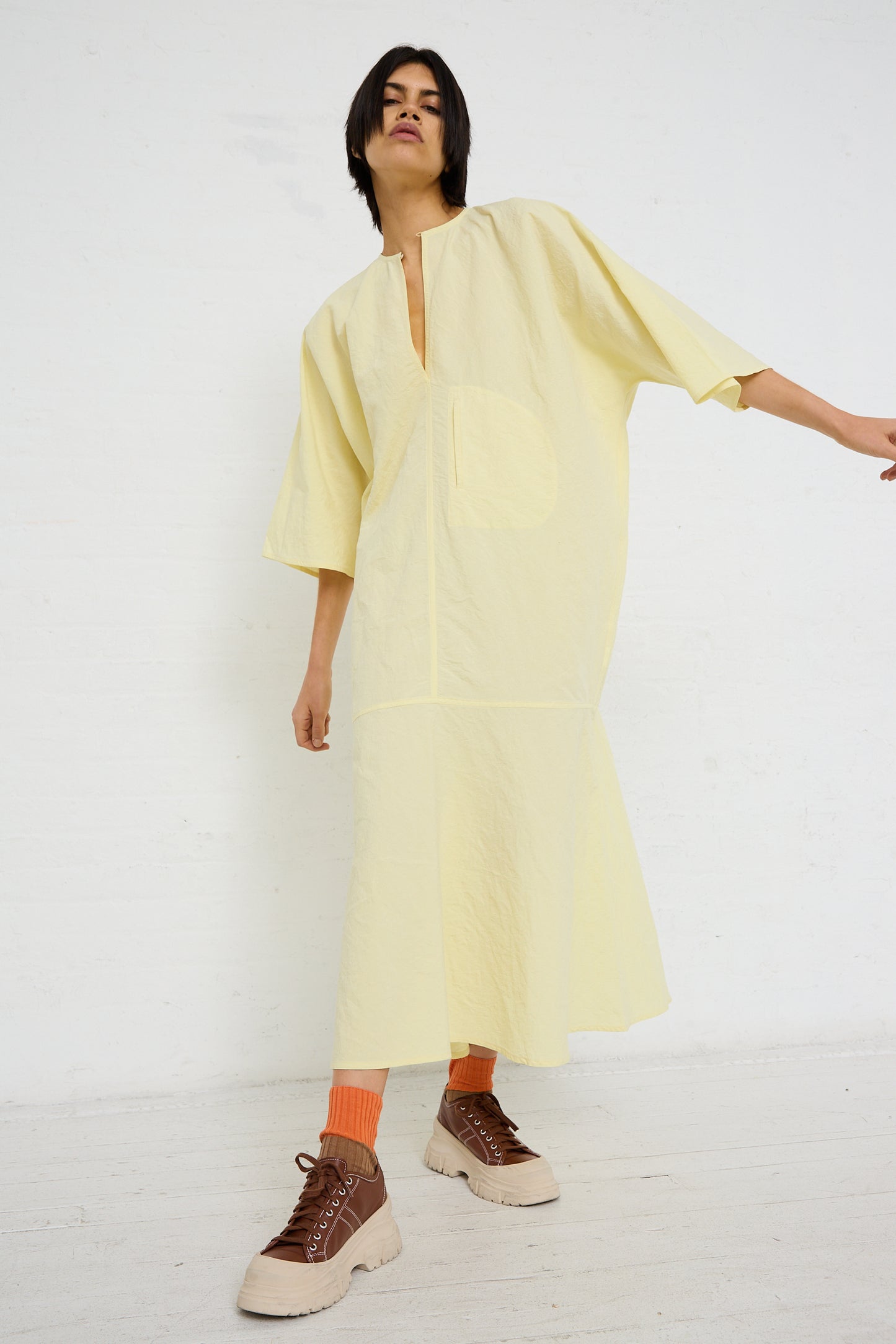 A person in a yellow oversized Linen Cotton Delfi Dress in Pastis made from Sofie D'Hoore, with pockets, posing in a white studio space.