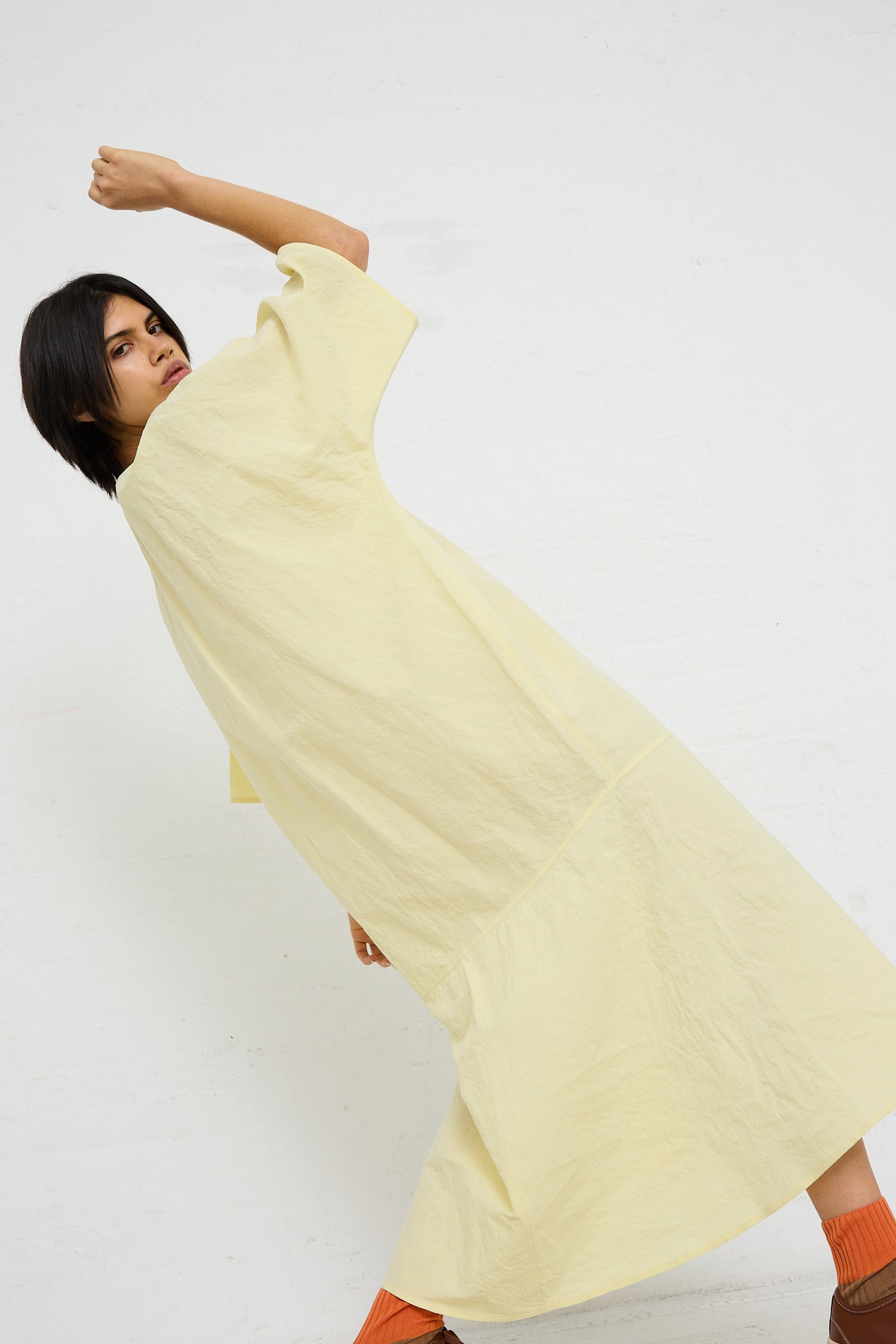 A person in a pale yellow oversized dress made from a sustainable Linen Cotton Delfi Dress in Pastis by Sofie D'Hoore, posing against a white background.