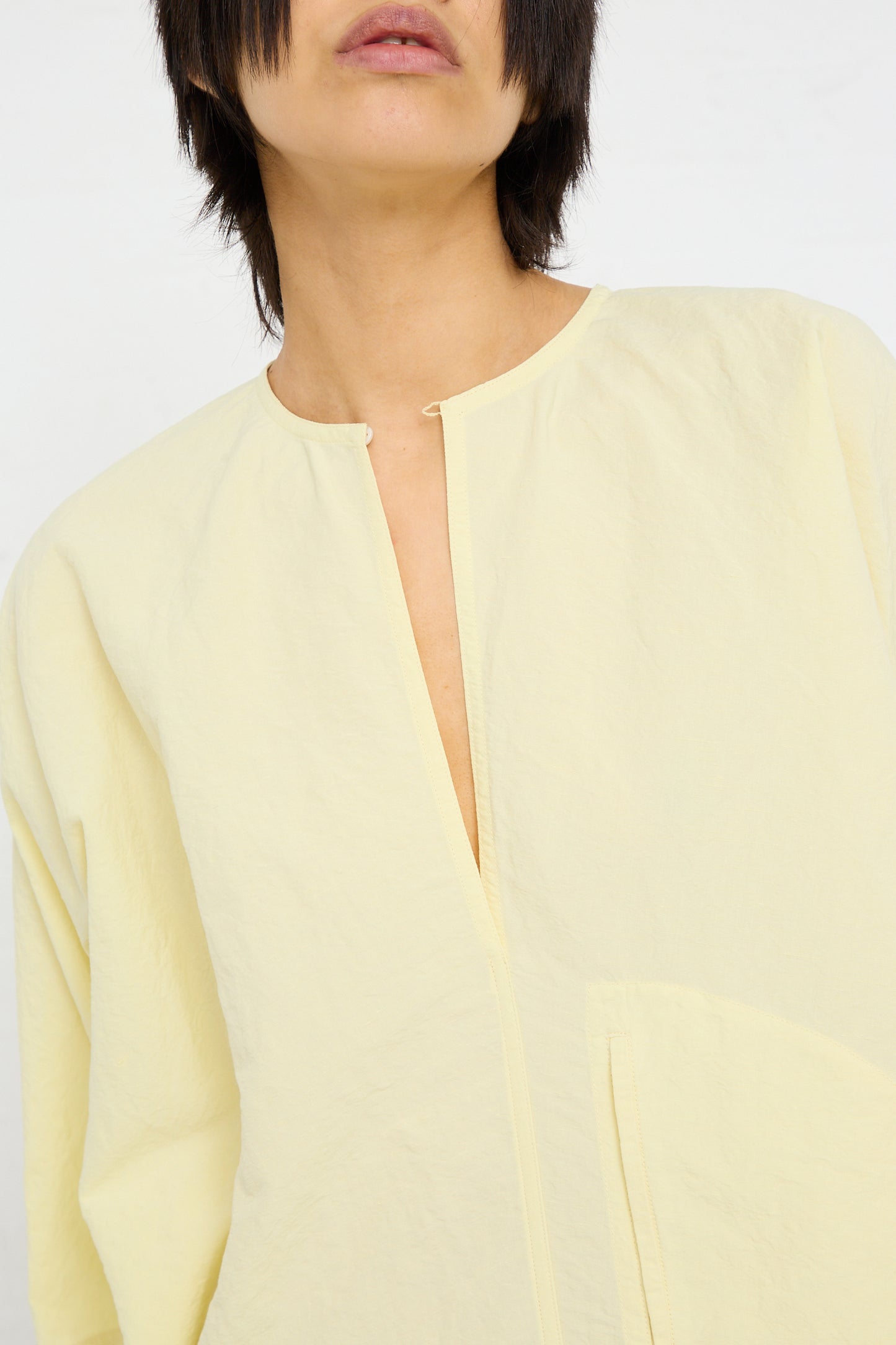 A person wearing an oversized yellow Linen Cotton Delfi Dress in Pastis made by Sofie D'Hoore, with a close-up on the neckline and upper chest.