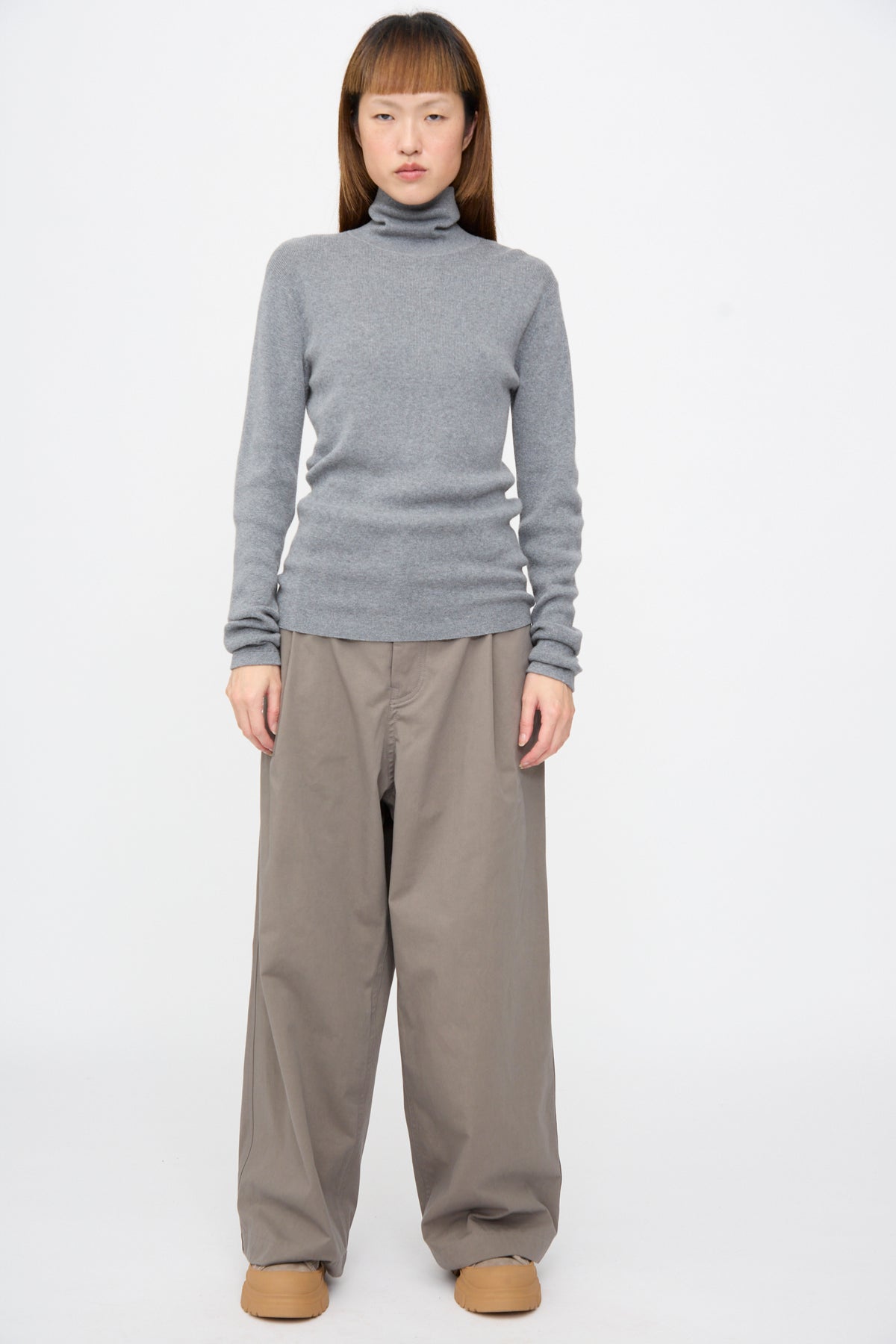 Person wearing a grey rib-knit Malika Sweater in Grey Melange, wide-leg taupe trousers, and tan platform shoes.