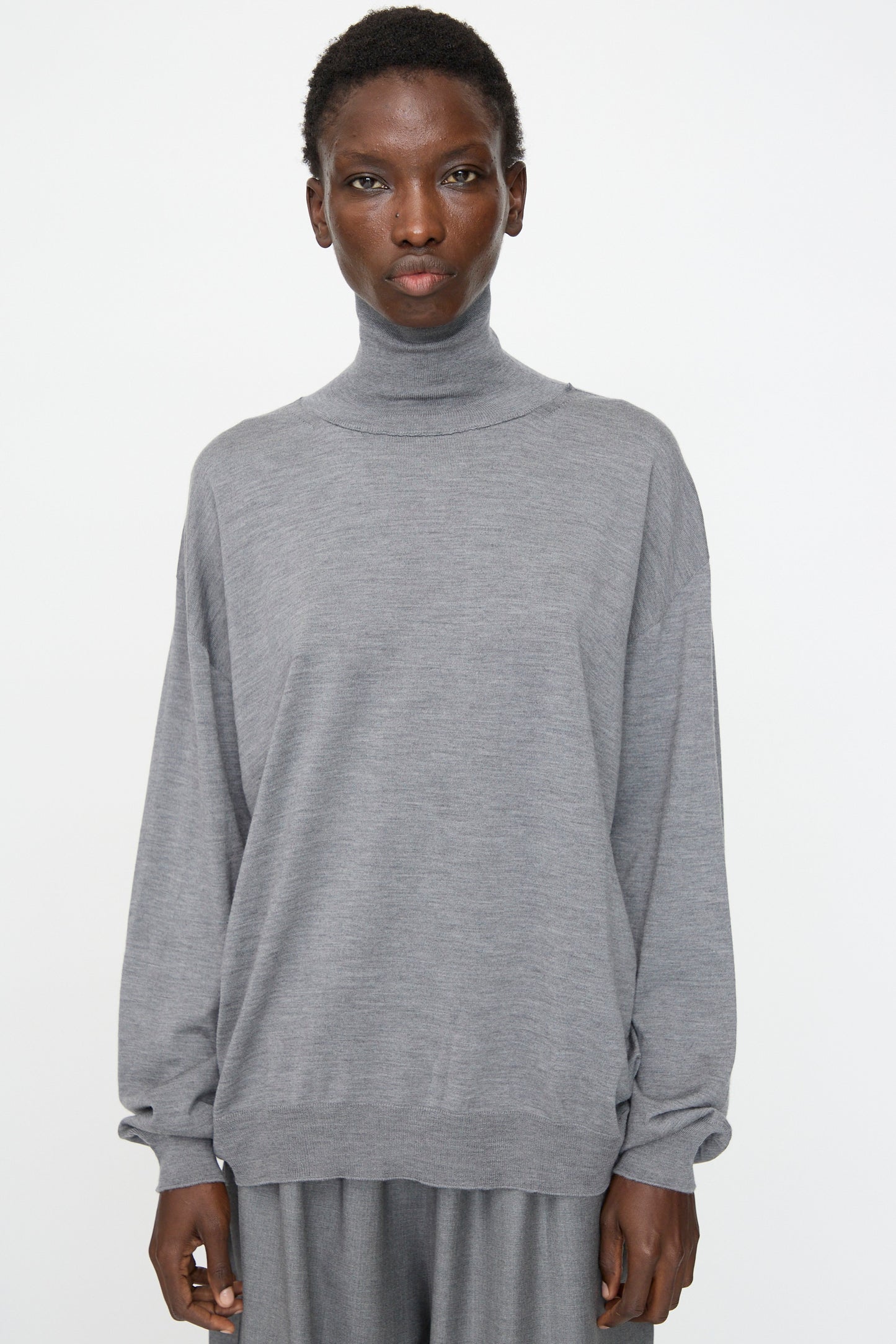 A person wearing the Sofie D'Hoore Merino Maffei Sweater in Steel Melange stands against a plain white background, paired with matching pants.